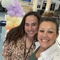 Two women smiling at a celebration with colorful balloons in the background.
