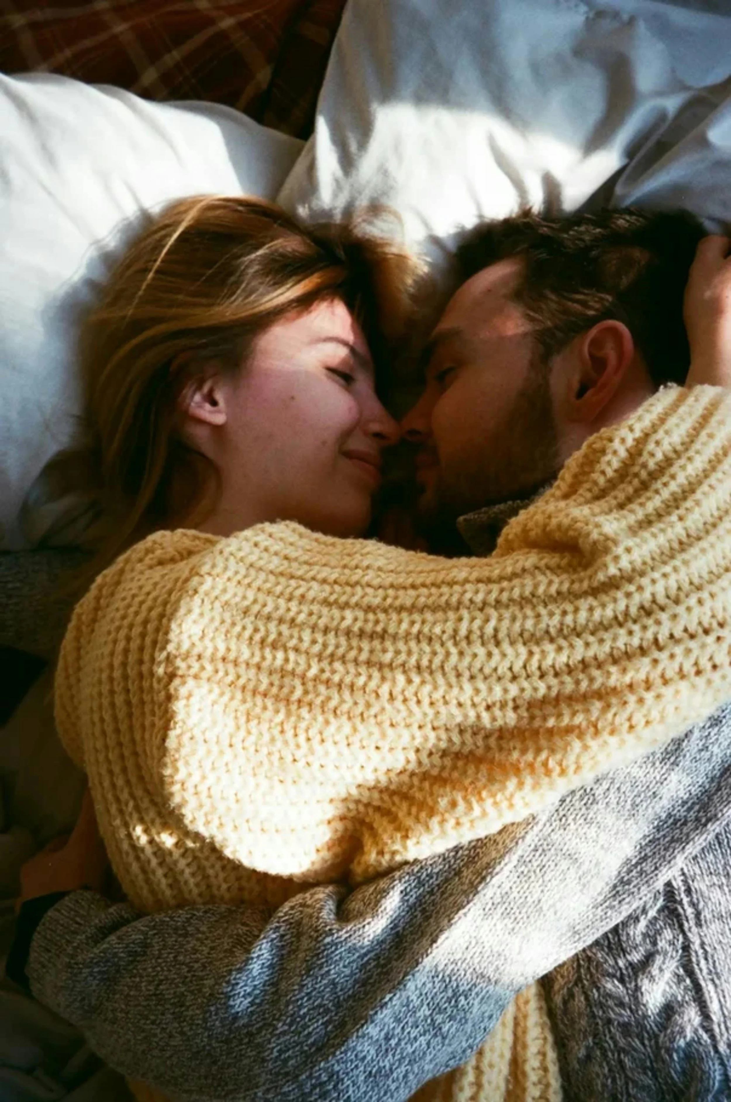 A couple lying in bed, cuddling and smiling at each other with their noses touching.