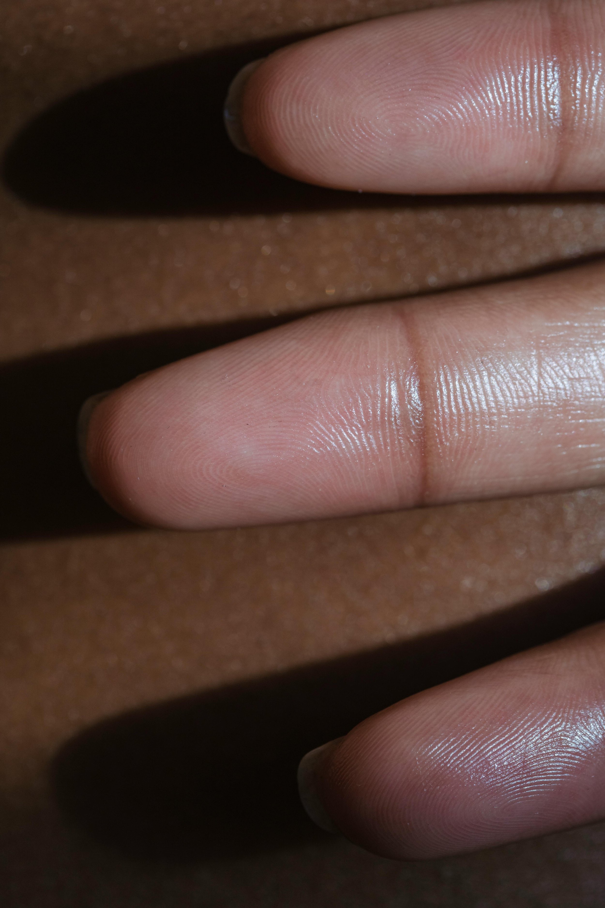 Close-up of fingers with detailed skin and fingerprint ridges, casting shadows on a brown textured surface.