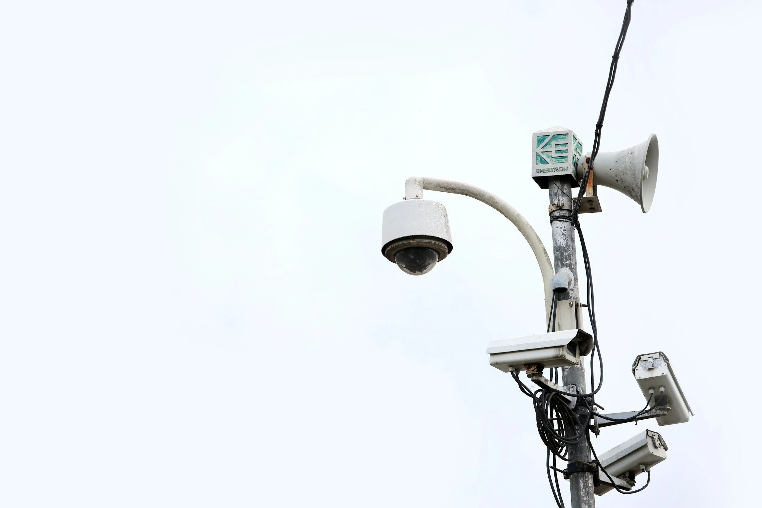 Security camera, loudspeaker, and surveillance equipment mounted on a pole against a cloudy sky.