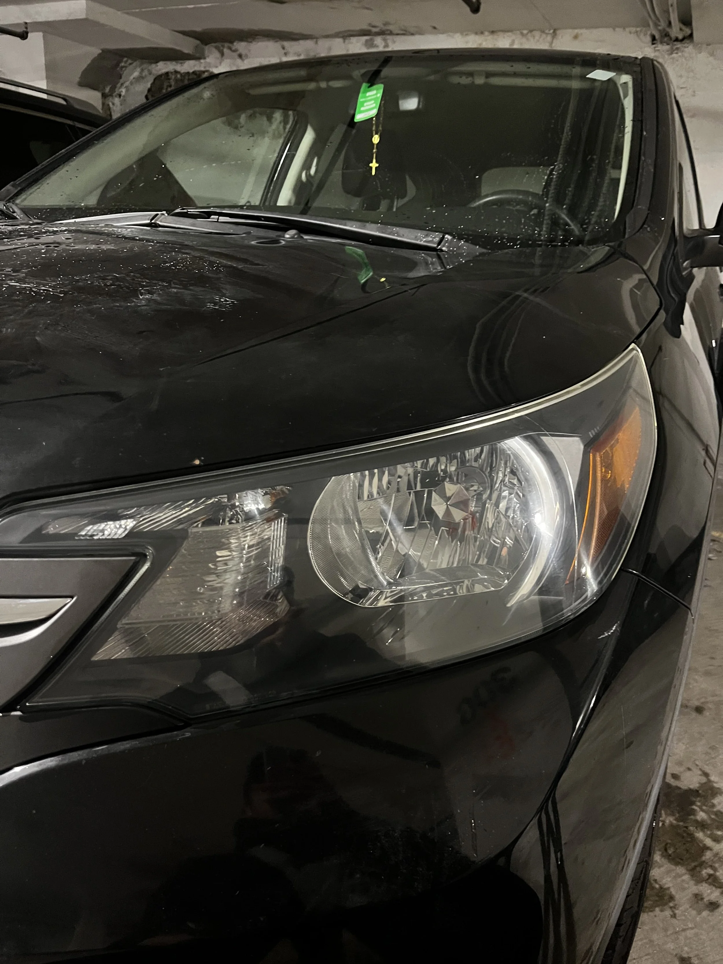 Black car parked in indoor parking lot, showing front left side, headlight, and windshield.