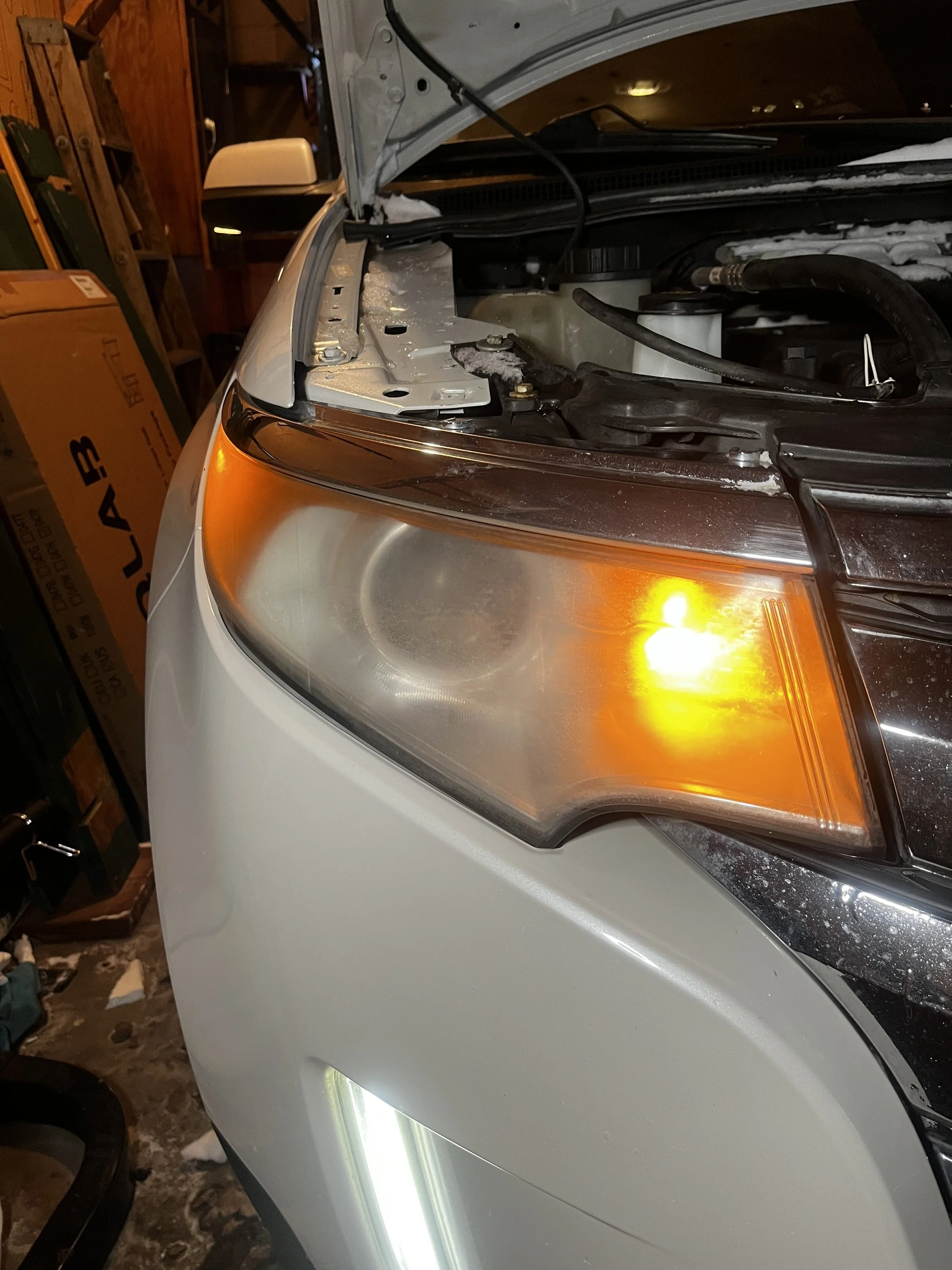 Front left side of car with open hood showing engine bay, headlight, and turn signal light.