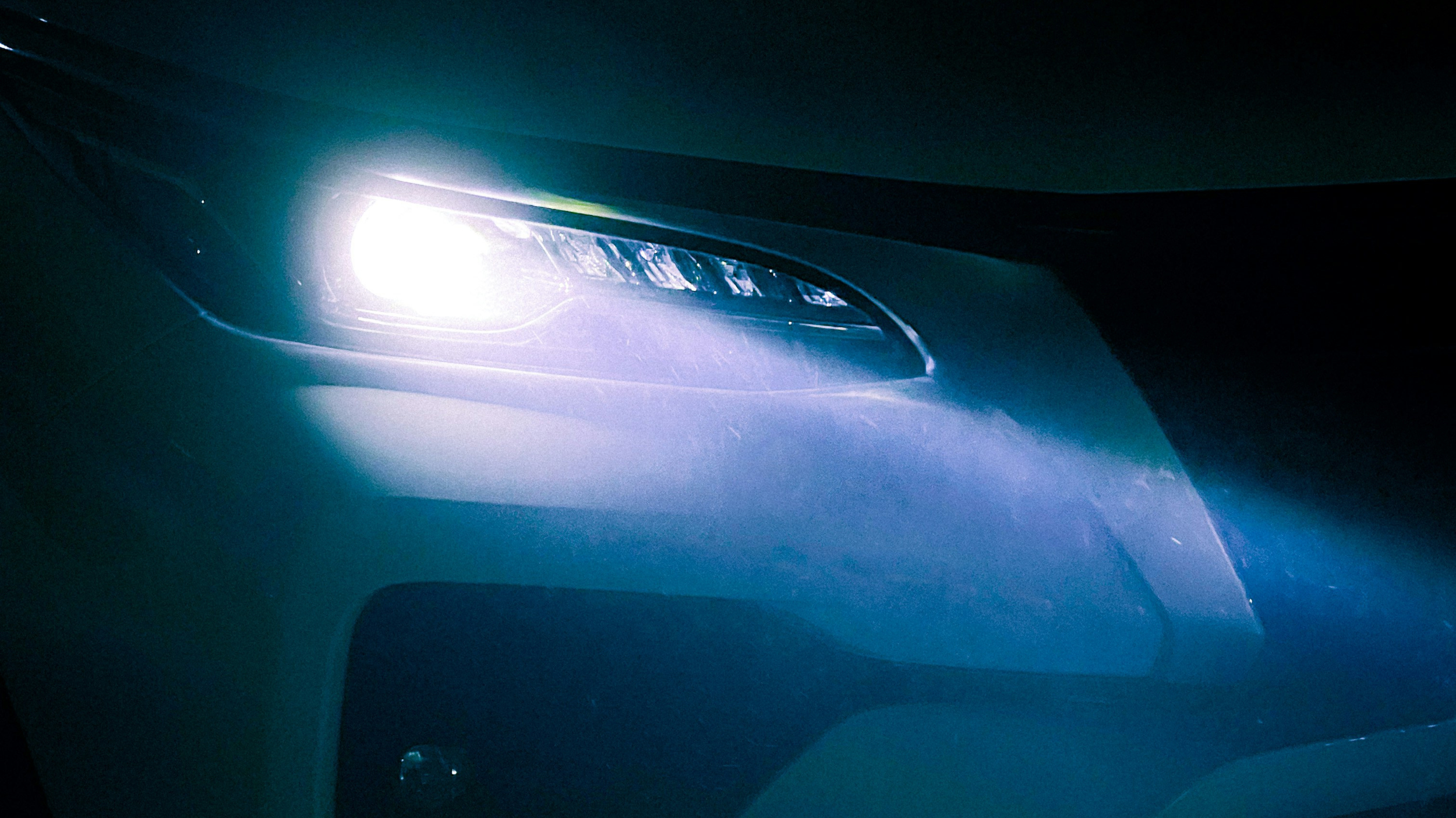 Close-up of a car's headlight at night, illuminated and shining brightly.