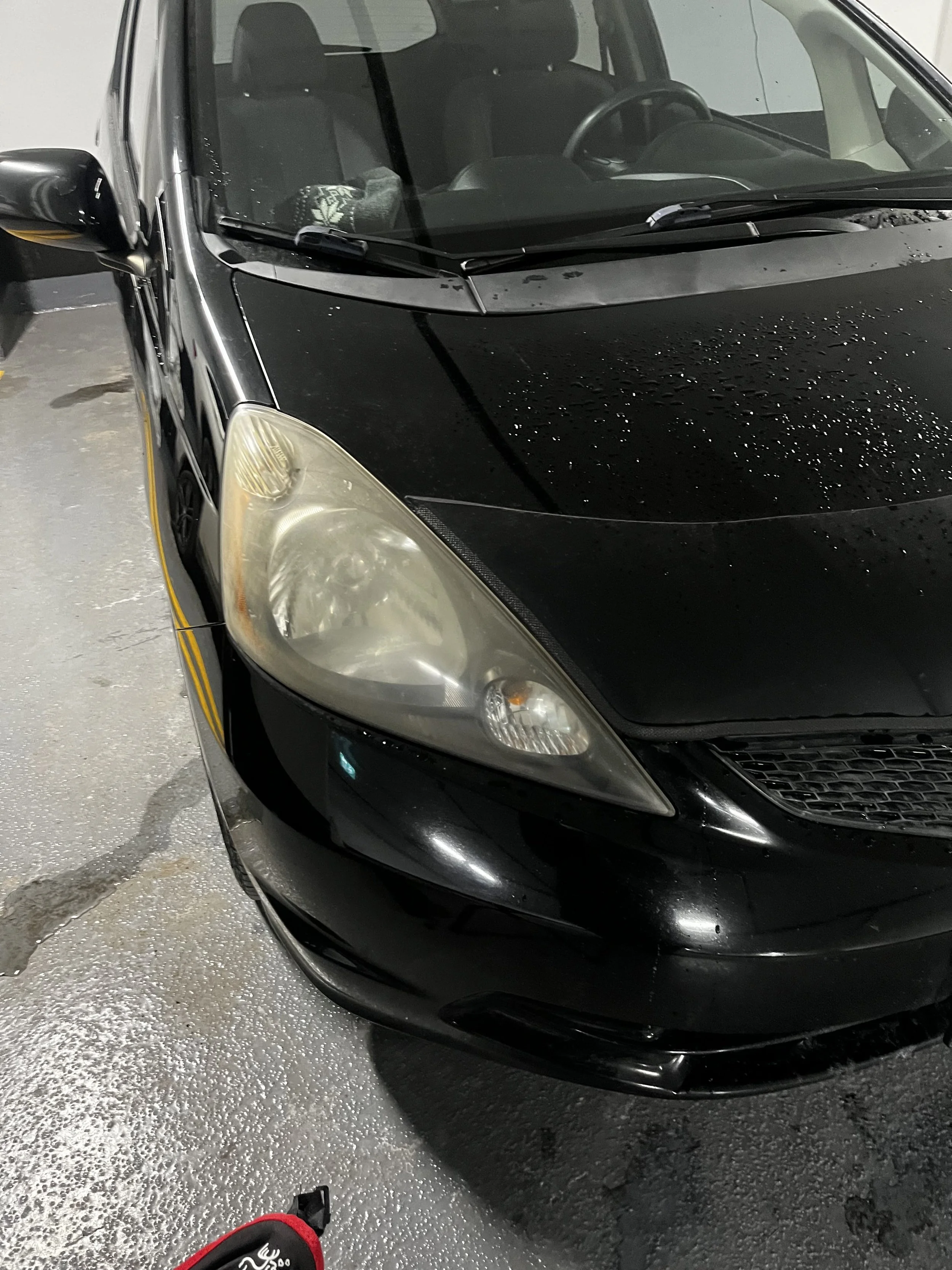 Black car parked in a parking lot with water droplets on its hood and a wet surface.