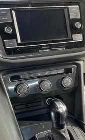 Inside a car, featuring a touchscreen display and climate control knobs below it, with a gear shift in front.