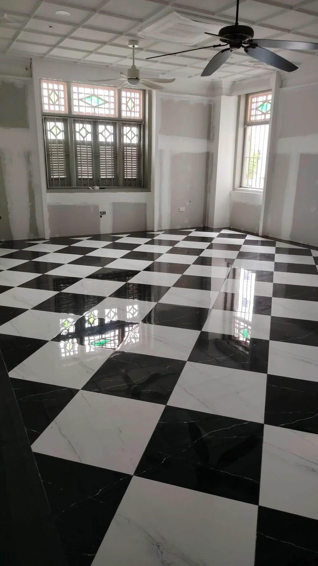 Empty room with black and white checkered marble floor, unfinished walls, and two ceiling fans.