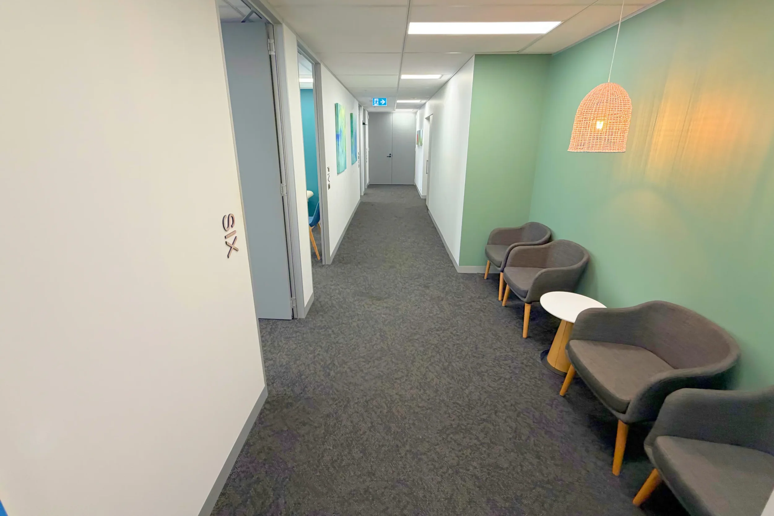 Clinic hallway at Naia Health St Leonards with patient seating, green feature wall and corridor to consultation rooms