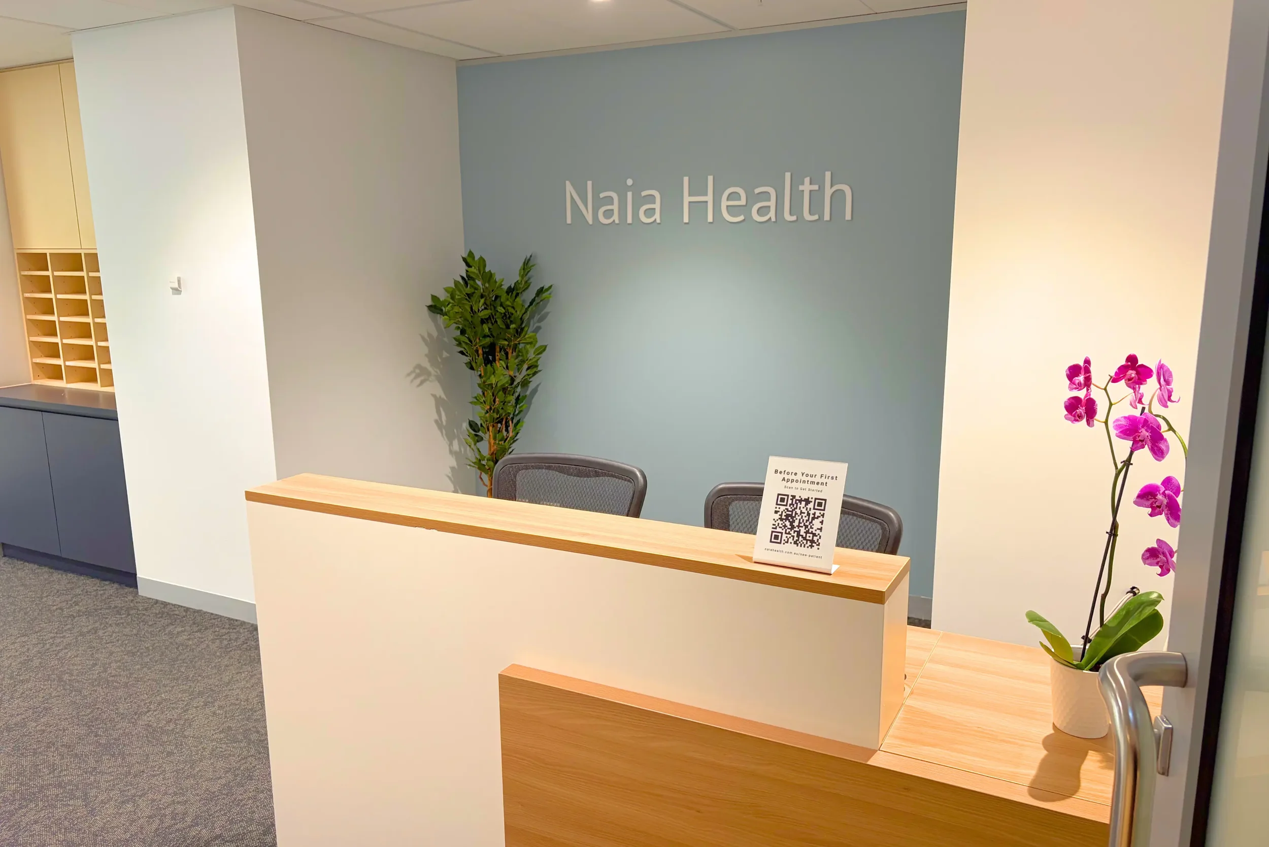 Reception desk at Naia Health specialist clinic in St Leonards Sydney with wooden reception counter, blue feature wall, orchid plant and patient check-in area