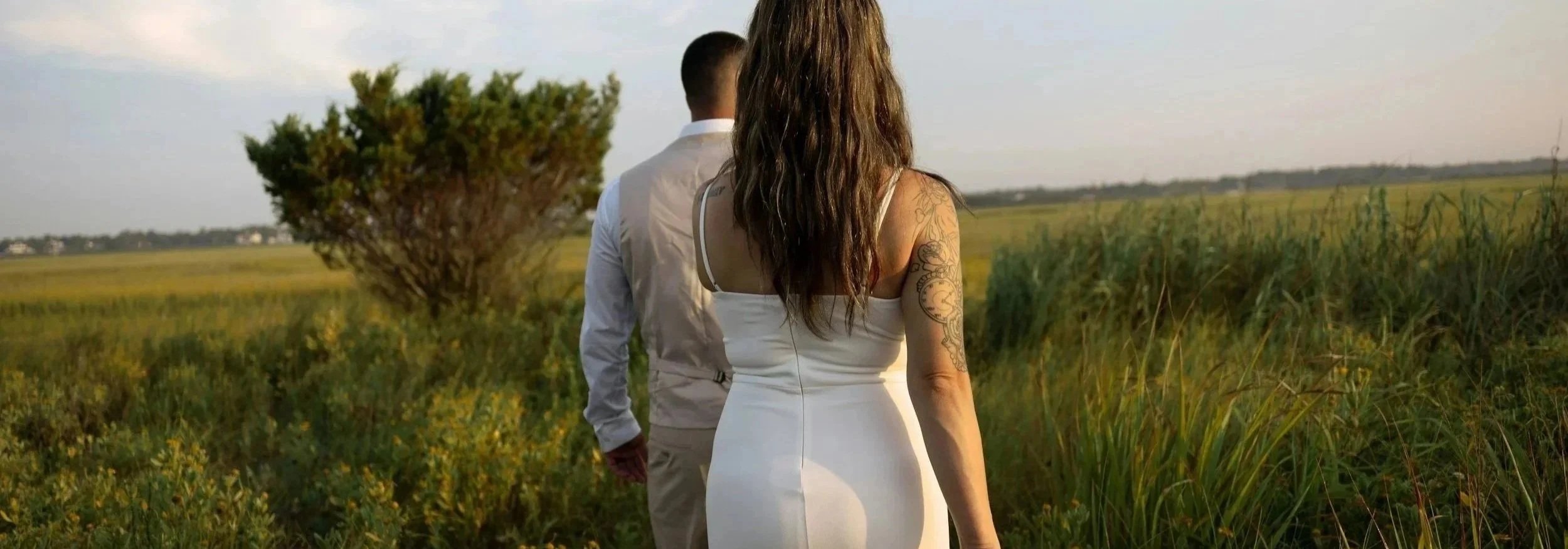 A bride with long curly hair and a tattoo on her left arm walking with her husband in western Washington