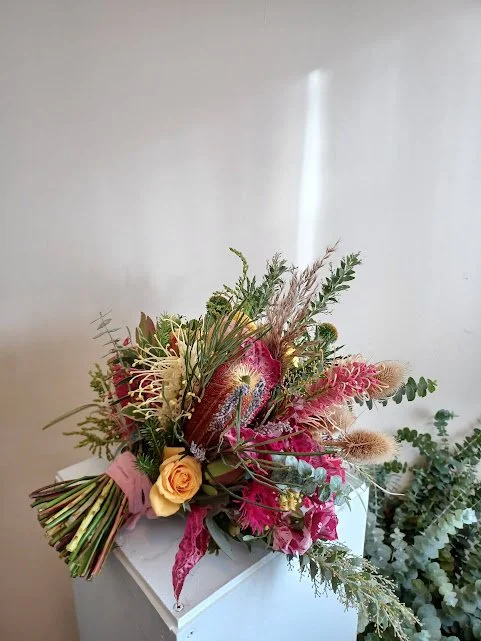 Colorful flower bouquet with pink, yellow, and green flowers and foliage, resting on a white surface.
