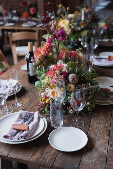 A decorated dining table with floral centerpiece, wine bottles, glasses, plates, and cutlery set for a meal.