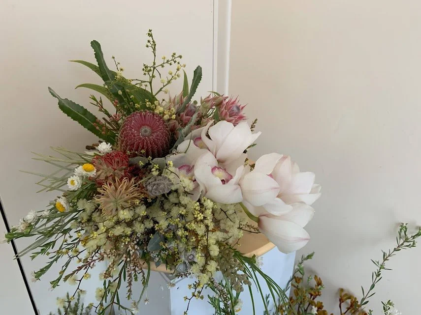 A floral arrangement with various flowers and greenery in a beige container.