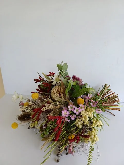 A colorful bouquet of various flowers and greenery arranged on a white surface against a plain white background.