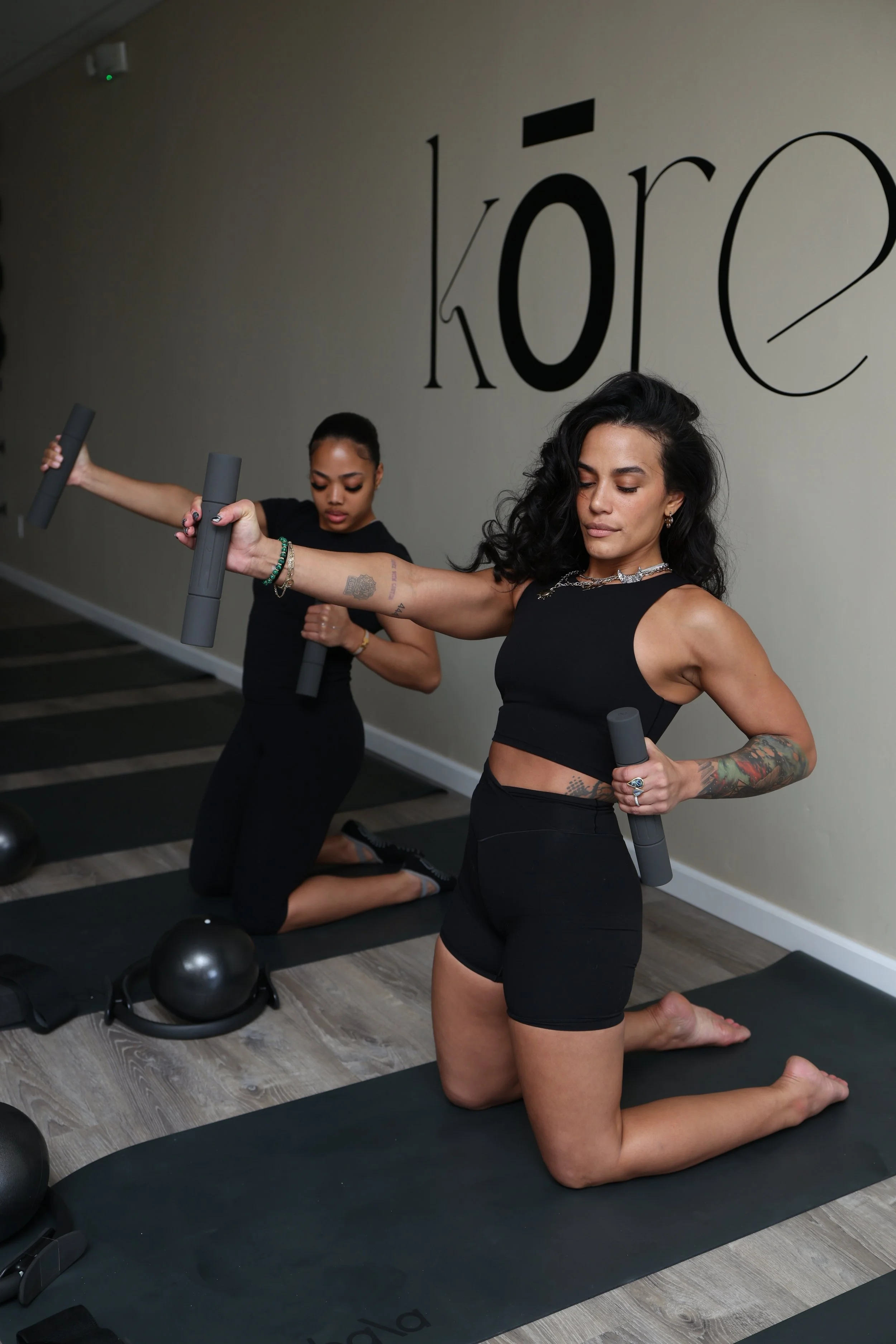 Two Kōre Mat Pilates Instructors practicing pilates at the Kōre Mat Pilates Studio, holding foam rollers in a kneeling position on pilates mats.