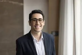 Smiling man with glasses in a suit standing indoors near a window