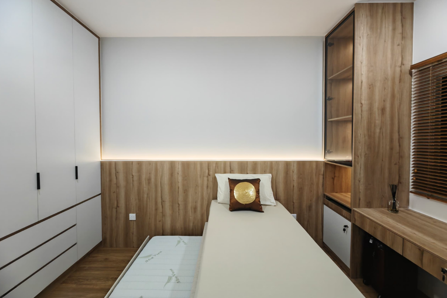 Bedroom with white and wood furniture, single bed with decorative cushion, built-in wardrobe, and window with wooden blinds.