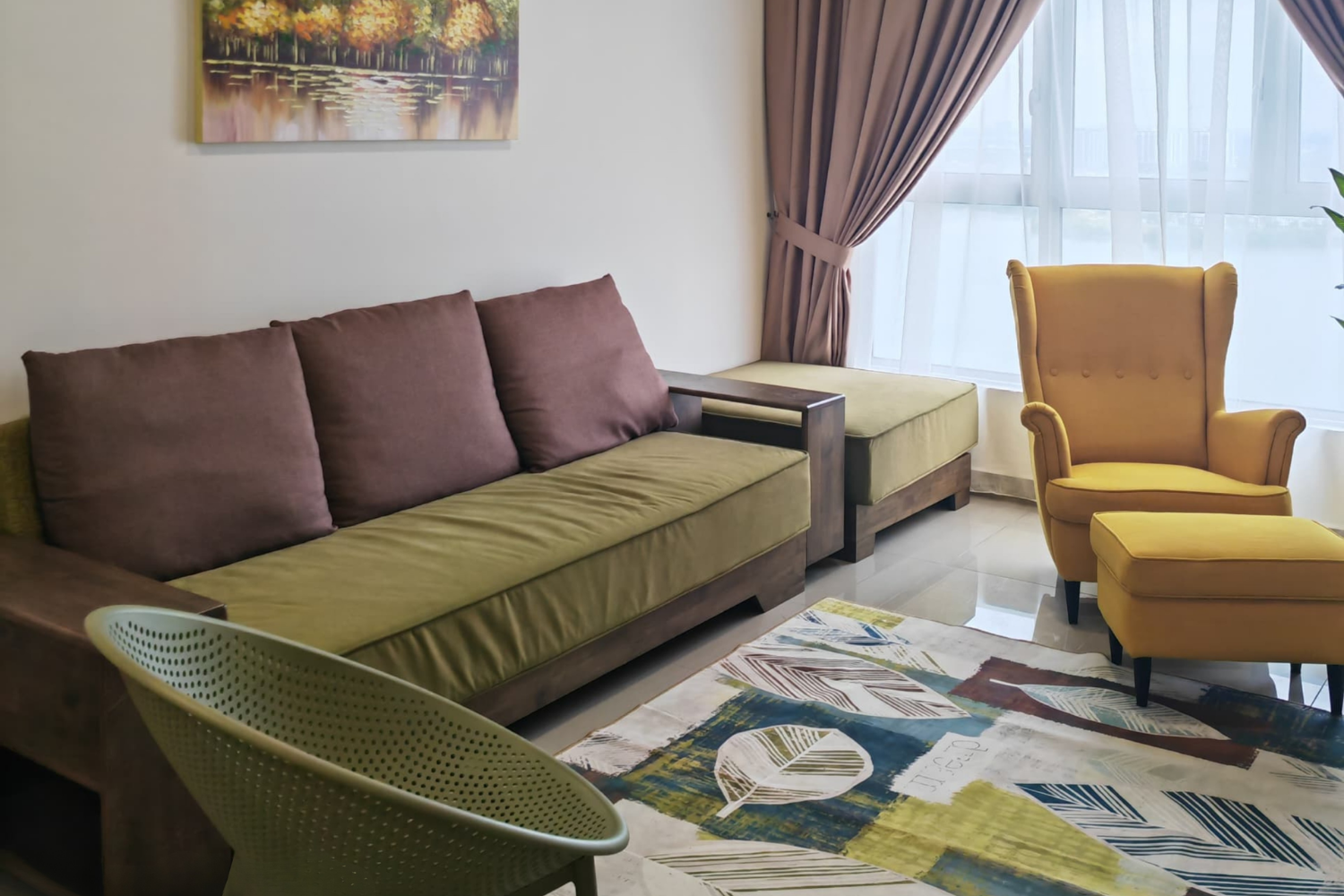 Living room with a green sofa and purple pillows, a yellow armchair with matching ottoman, a colorful leaf-patterned rug, and a window with pink curtains.