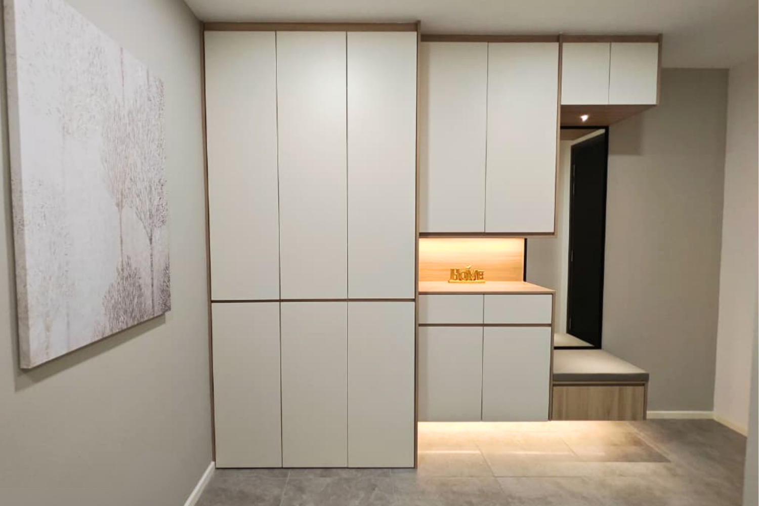 Modern interior with large white storage cabinets, a built-in wooden bench with cushion, and a wall art piece depicting trees.