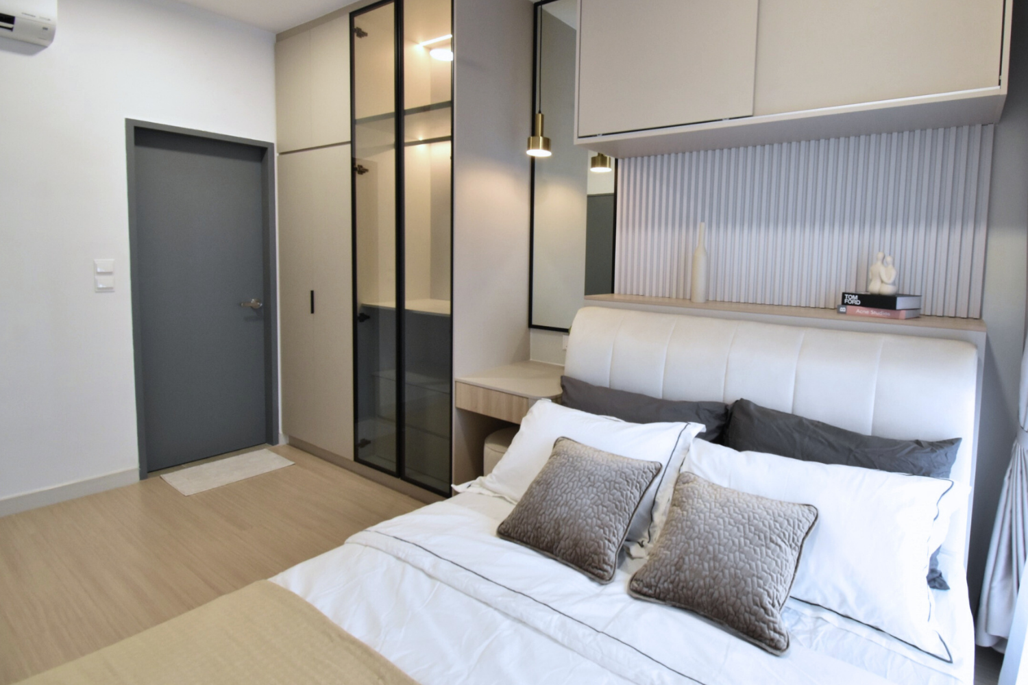Modern bedroom with a white bed, gray pillows, a built-in wall cabinet with decorative items and books, and a gray door.