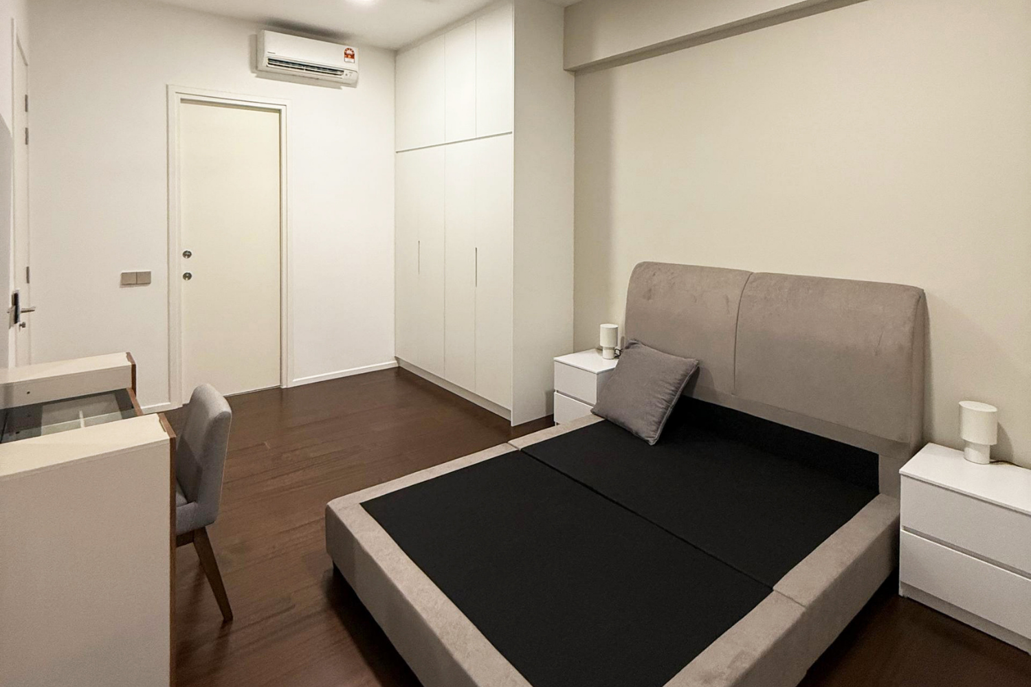 A minimalist bedroom with a bed, two bedside tables with lamps, a gray headboard, a white wardrobe, and a wall-mounted air conditioning unit