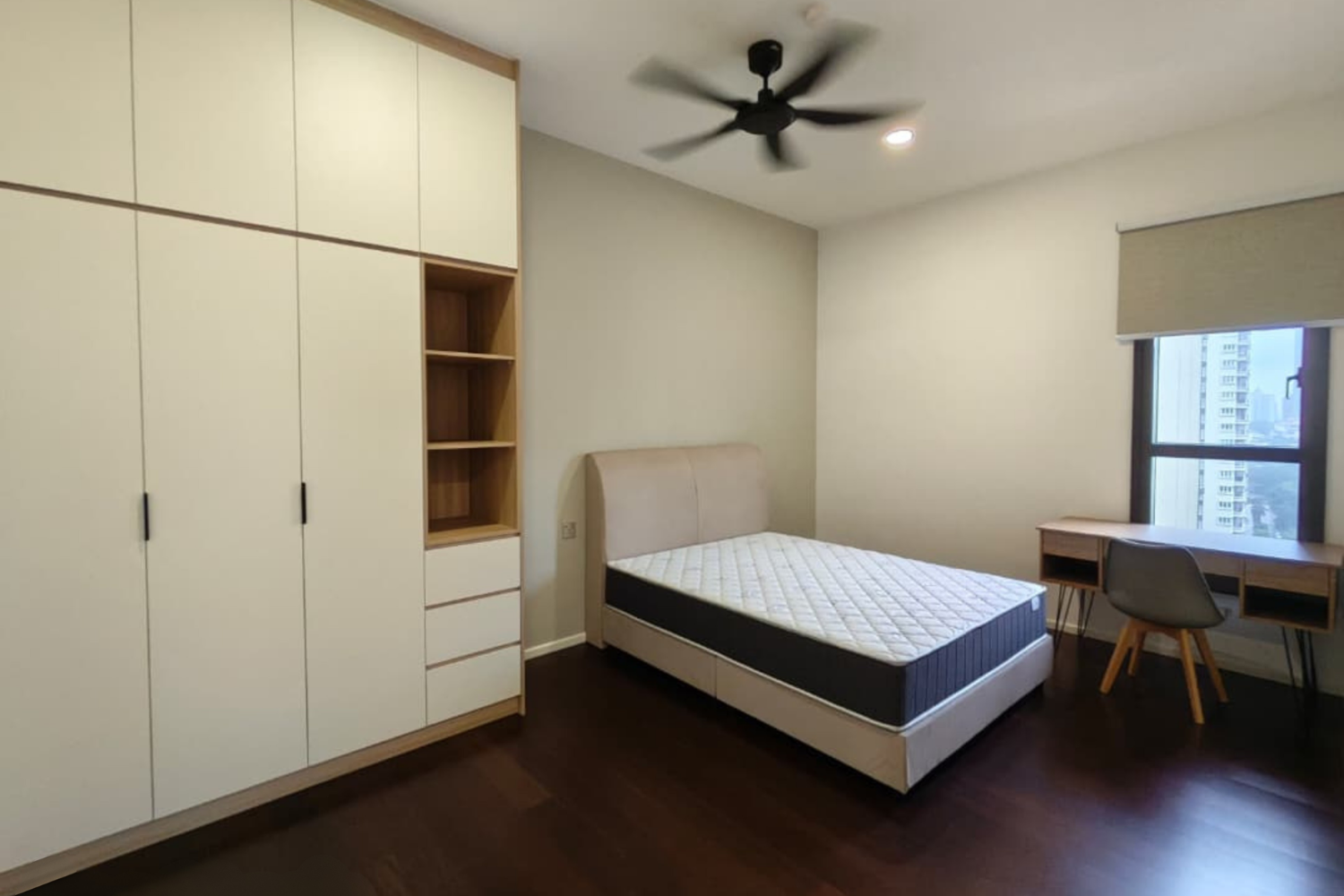 A minimalist bedroom with a bed, a large wardrobe with open shelf, a small desk near the window, a modern chair, and a ceiling fan.