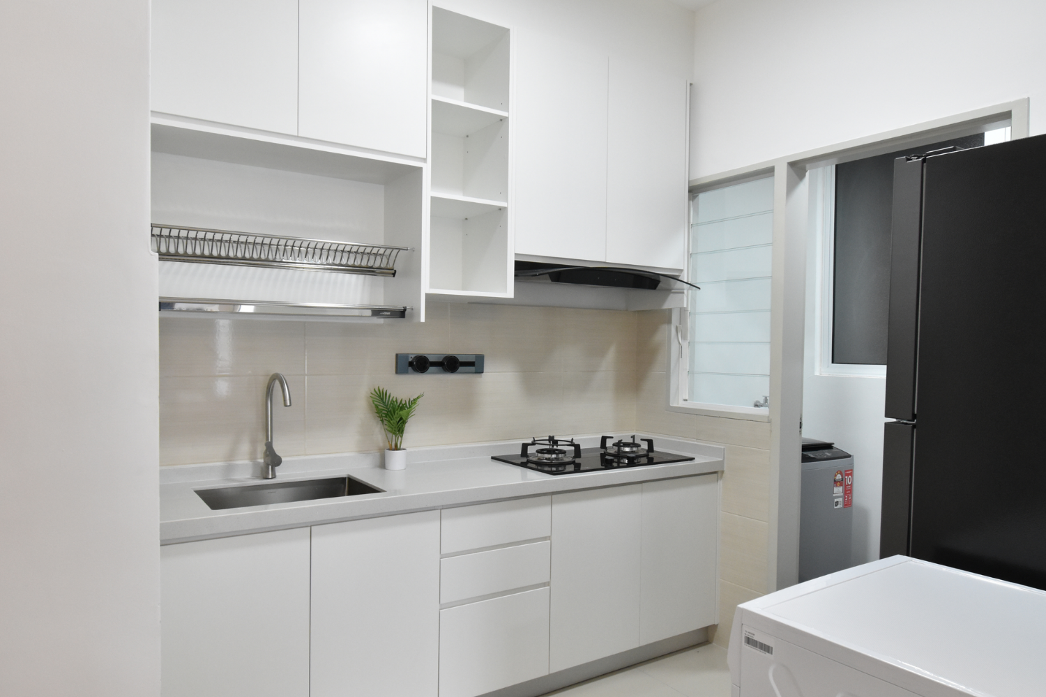 Modern kitchen with white cabinets, a sink, a stove with two burners, and black refrigerator. There's a small potted plant on the counter and a window above the stove.