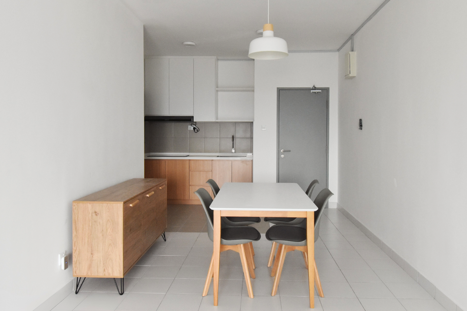 Minimalist kitchen and dining area with a white table, six black chairs, a wooden sideboard, white cabinets, gray door, and a white pendant light.
