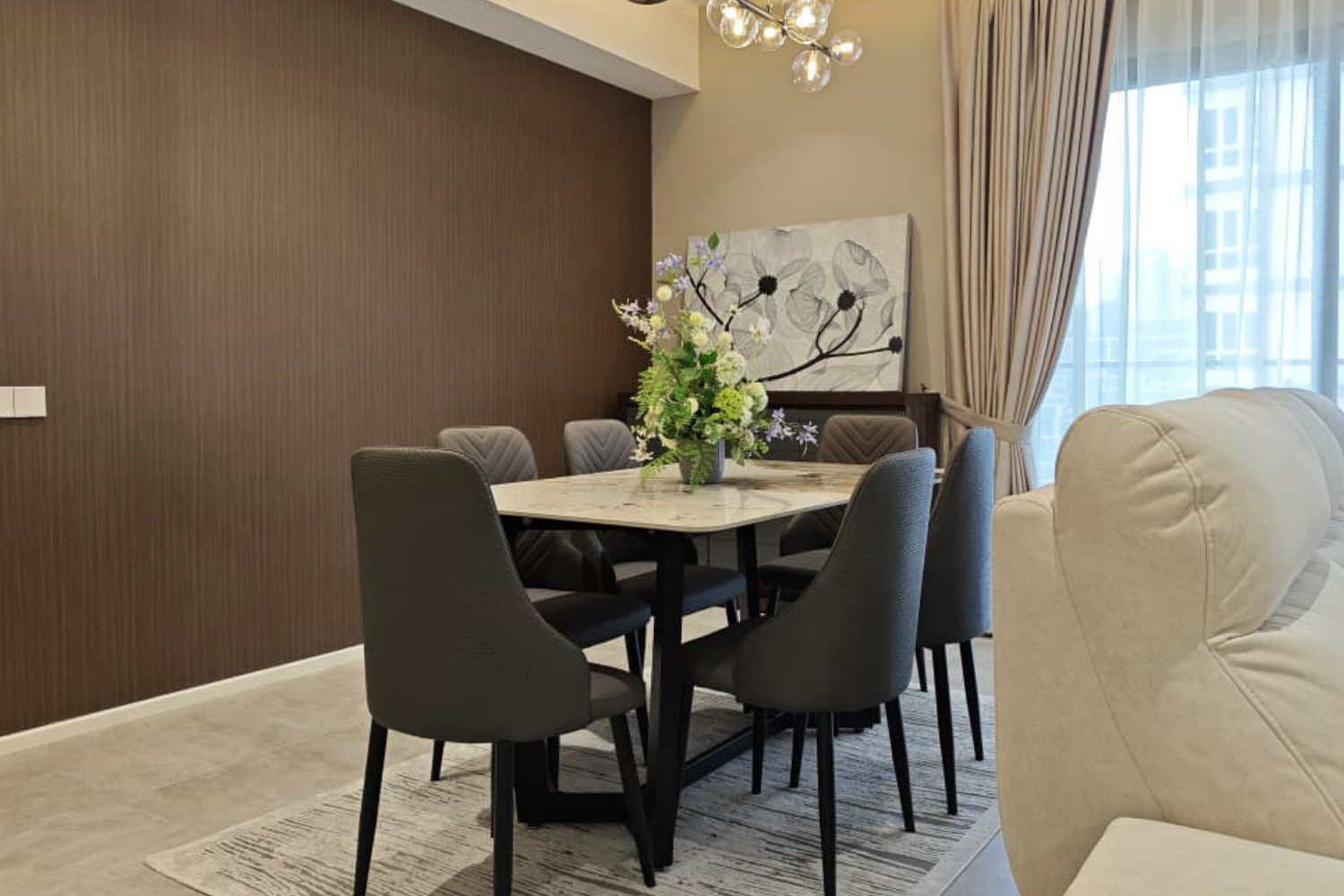 Modern dining room with a marble table, six black chairs, a floral centerpiece, a textured brown accent wall, a large abstract artwork, and a glass pendant light fixture.