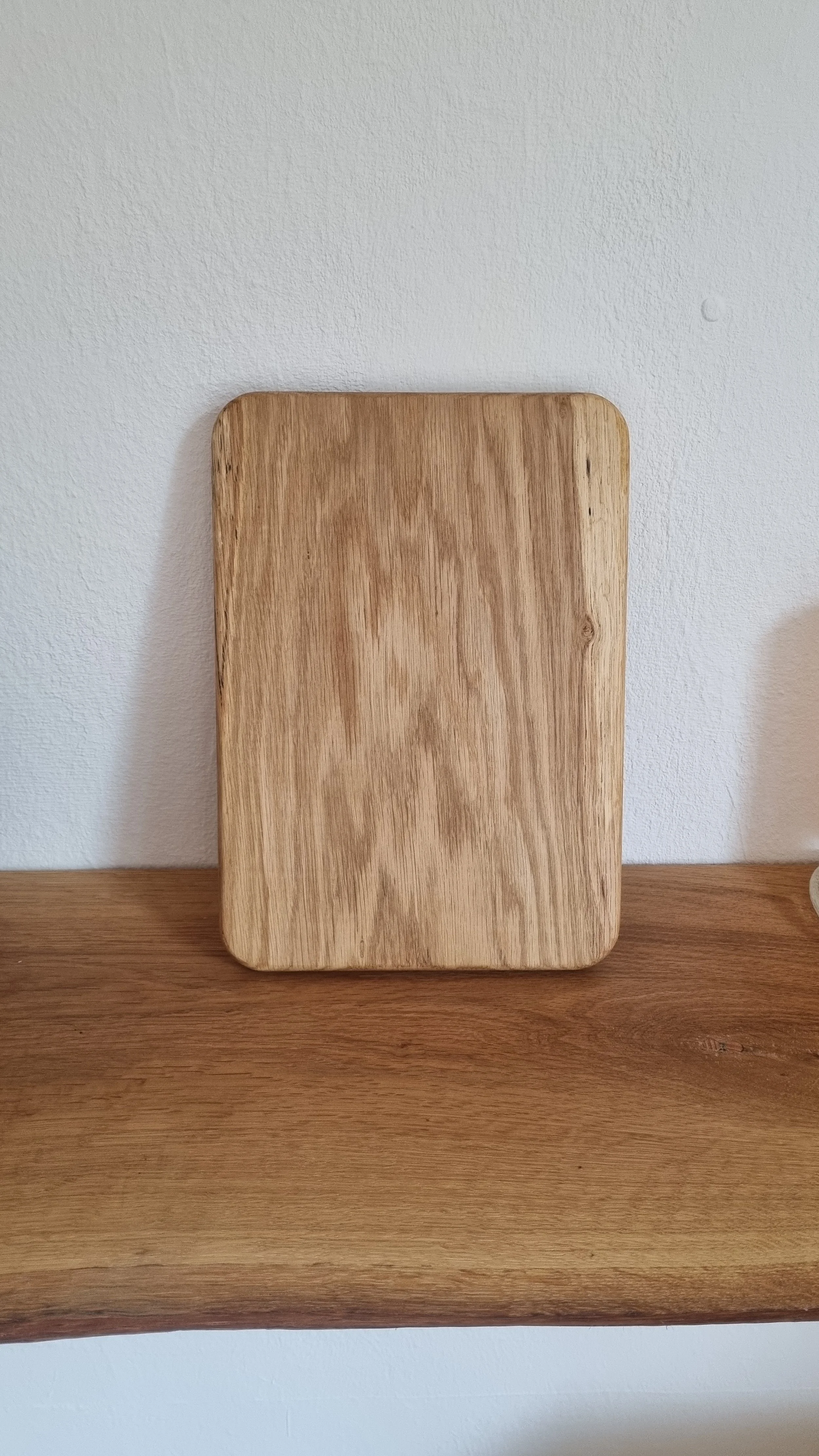 Ein hölzernes Schneidebrett auf einem Holztisch vor einer weißen Wand.