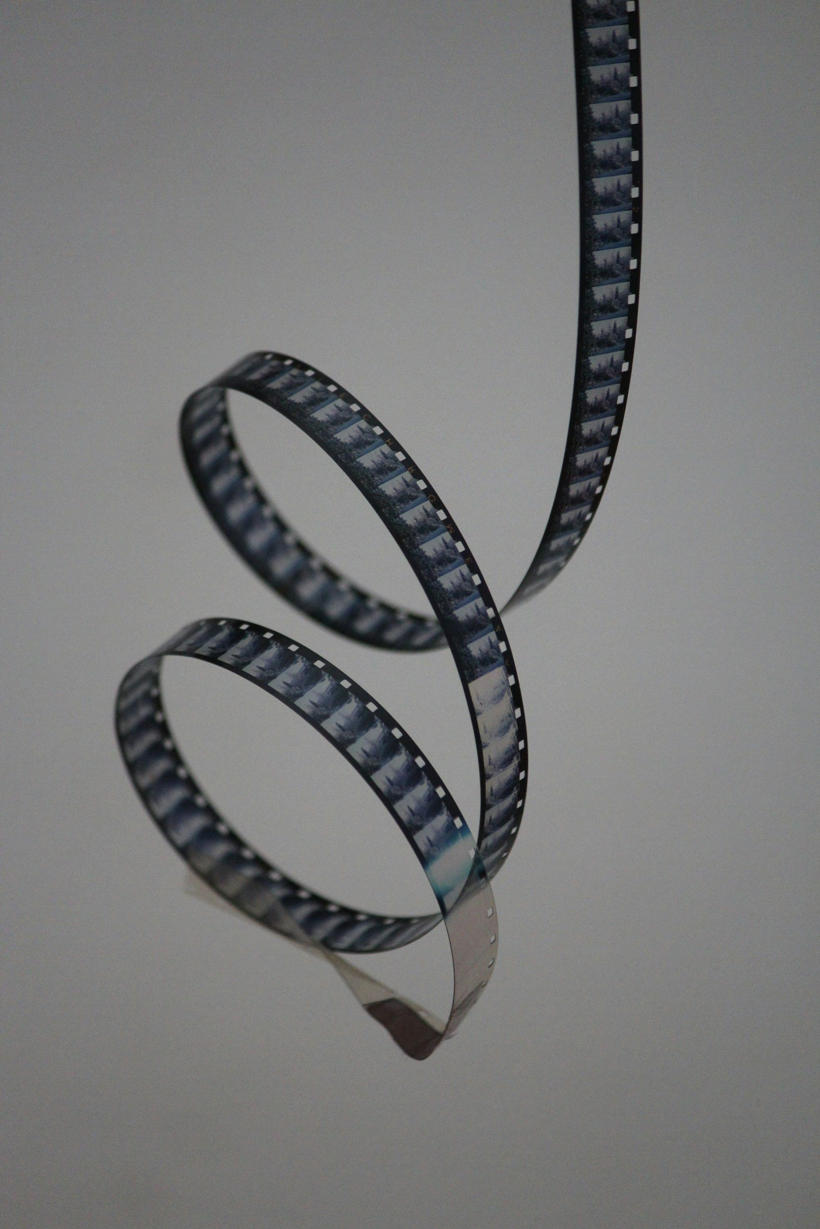 A strip of photographic film curled in a spiral, hanging against a plain background.
