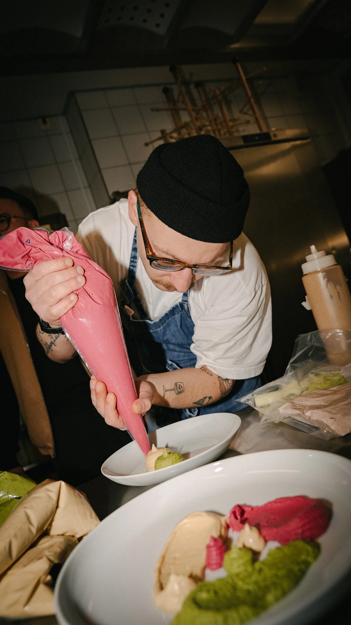 Chef decorating a dish with pink sauce in a professional kitchen.