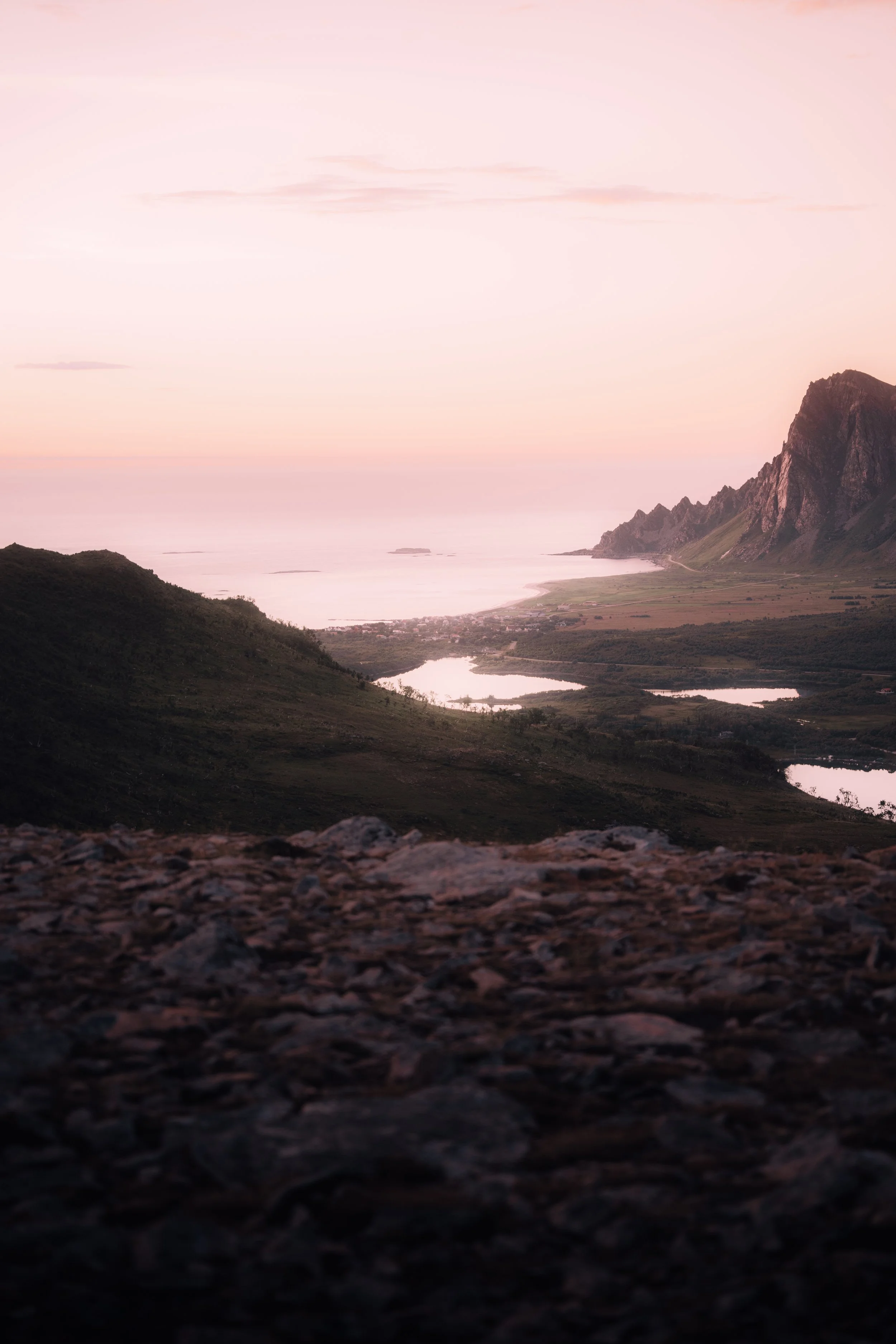Näky vuoristomaisemasta auringonlaskun aikaan, näköala vuoristosta ja järvestä, taivaan värjääntyessä vaaleanpunaiseksi.
