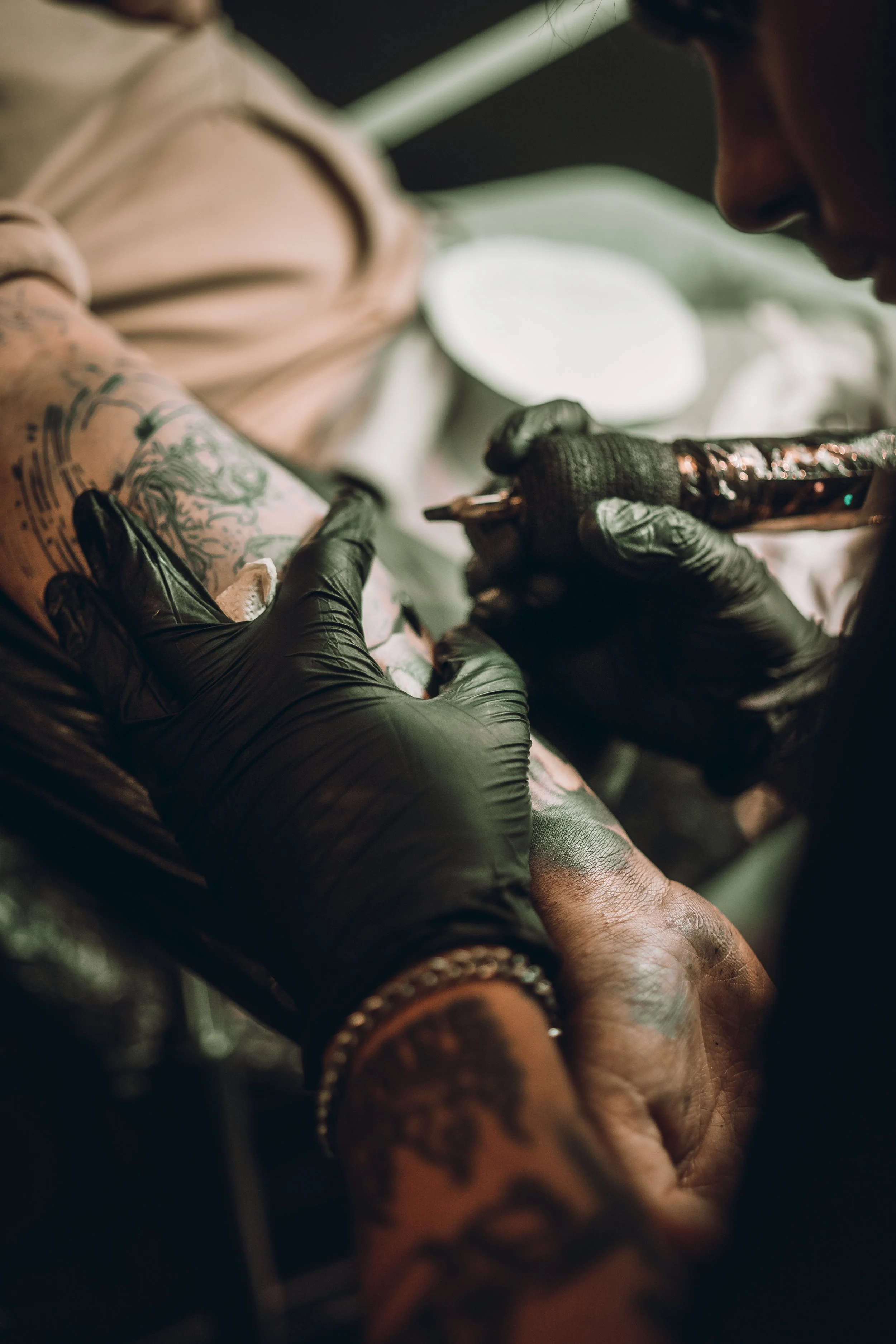 Kuvassa tatuoija tekee tatuointia asiakkaan käsivarteen. Tatuoija käyttää suojakäsineitä ja töhertää ihon päälle.