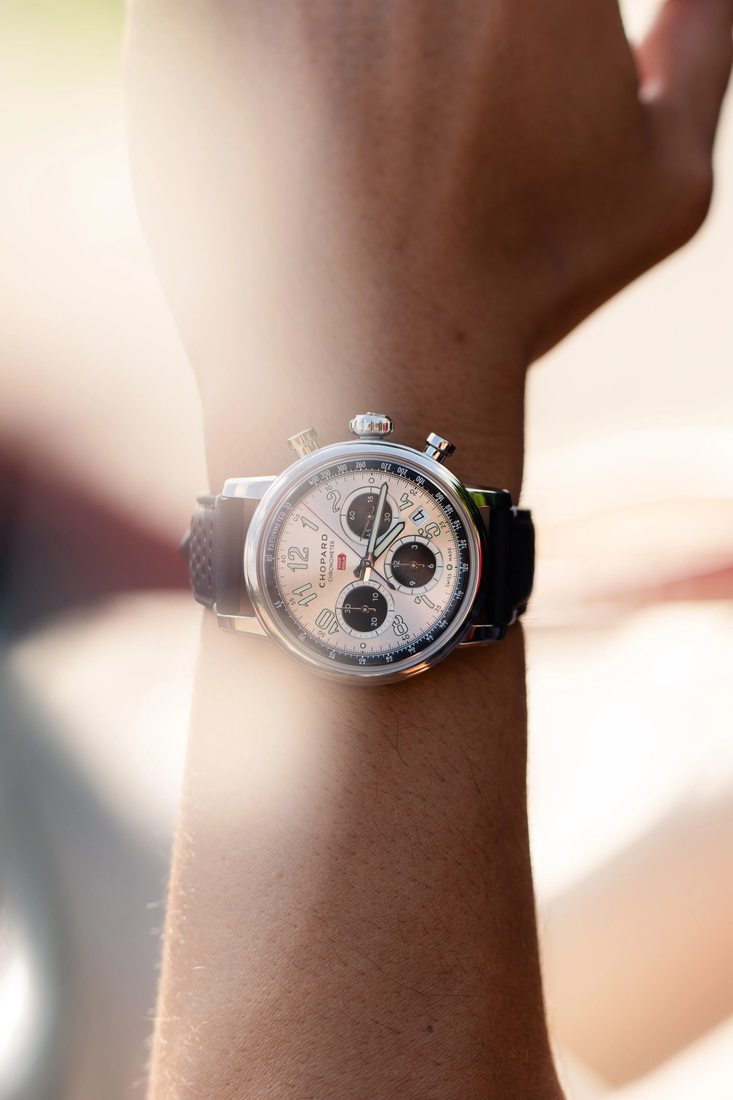 Montre chronographe de marque Chopard sur un poignet, avec un cadran blanc, des sous-compteurs noirs, des aiguilles argentées et un bracelet en cuir noir.