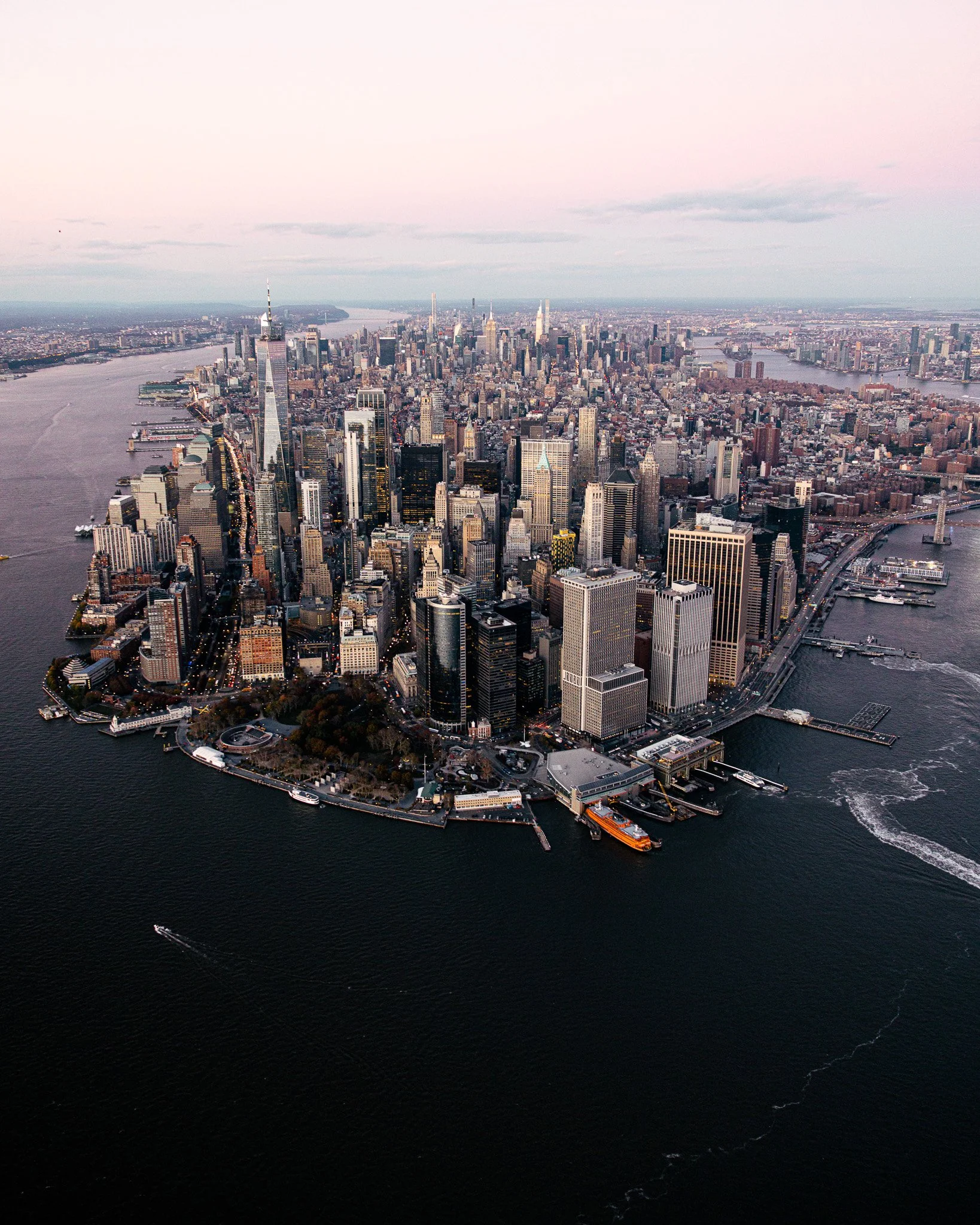 La skyline de Manhattan avec de nombreux gratte-ciel, située sur une île entourée d'eau, prise depuis les airs au coucher du soleil.