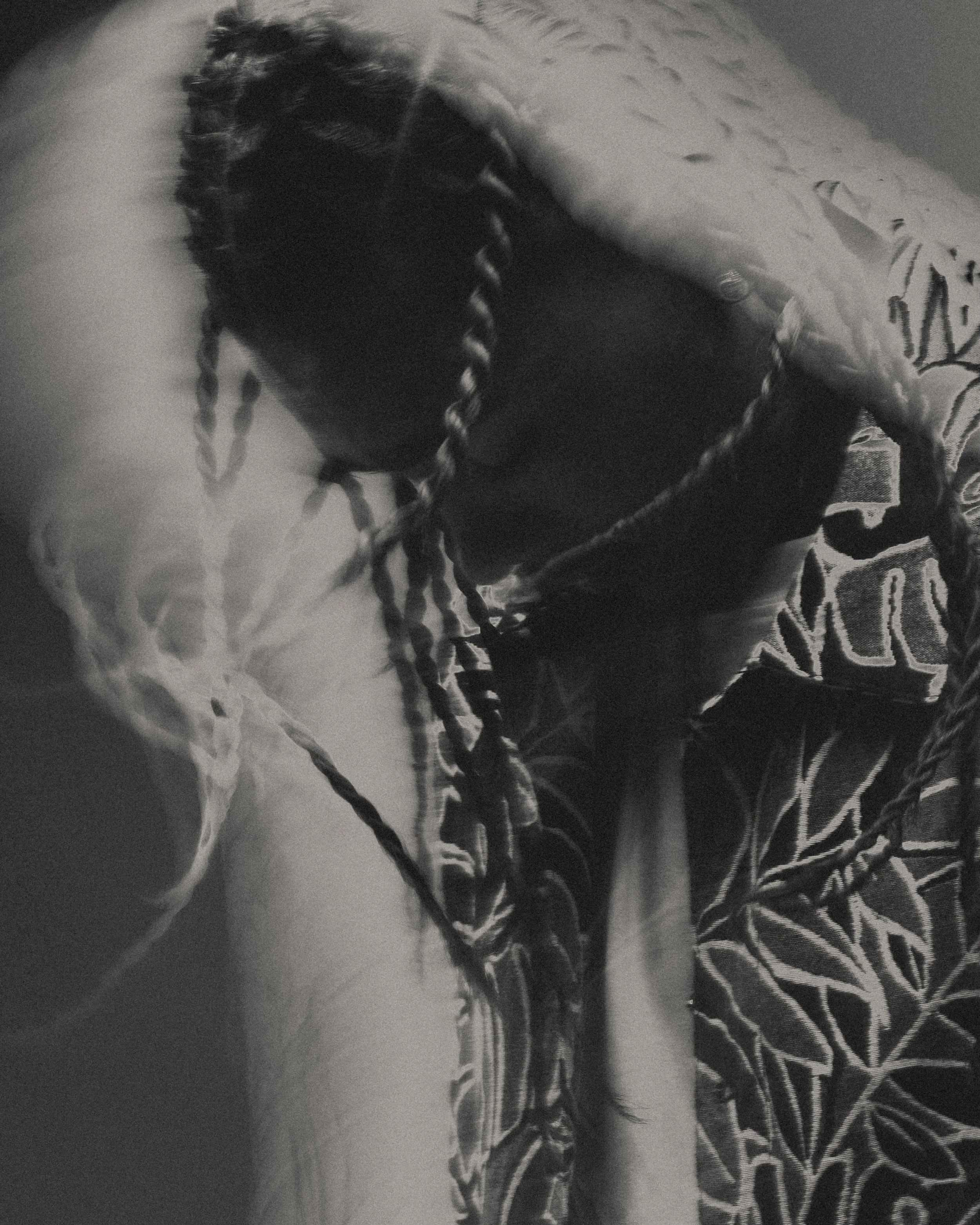 Une personne à cheveux tressés repose sur un canapé orné de coussins à motifs végétaux.