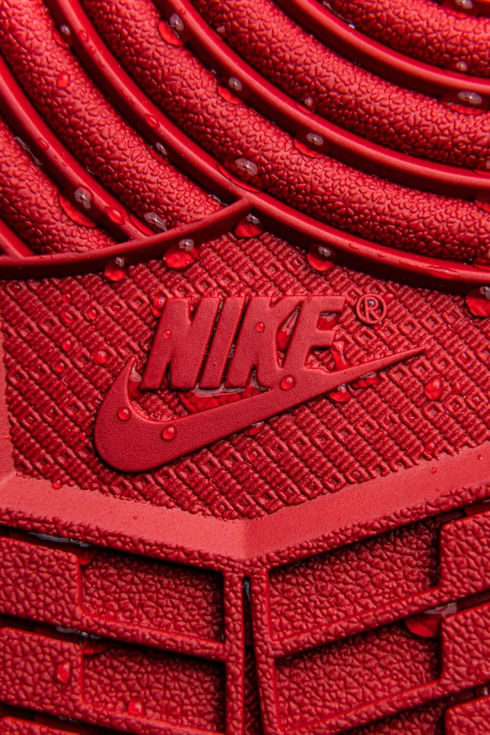 Détail en gros plan d'une chaussure Nike rouge, avec gouttes d'eau sur la surface et le logo Nike en relief.