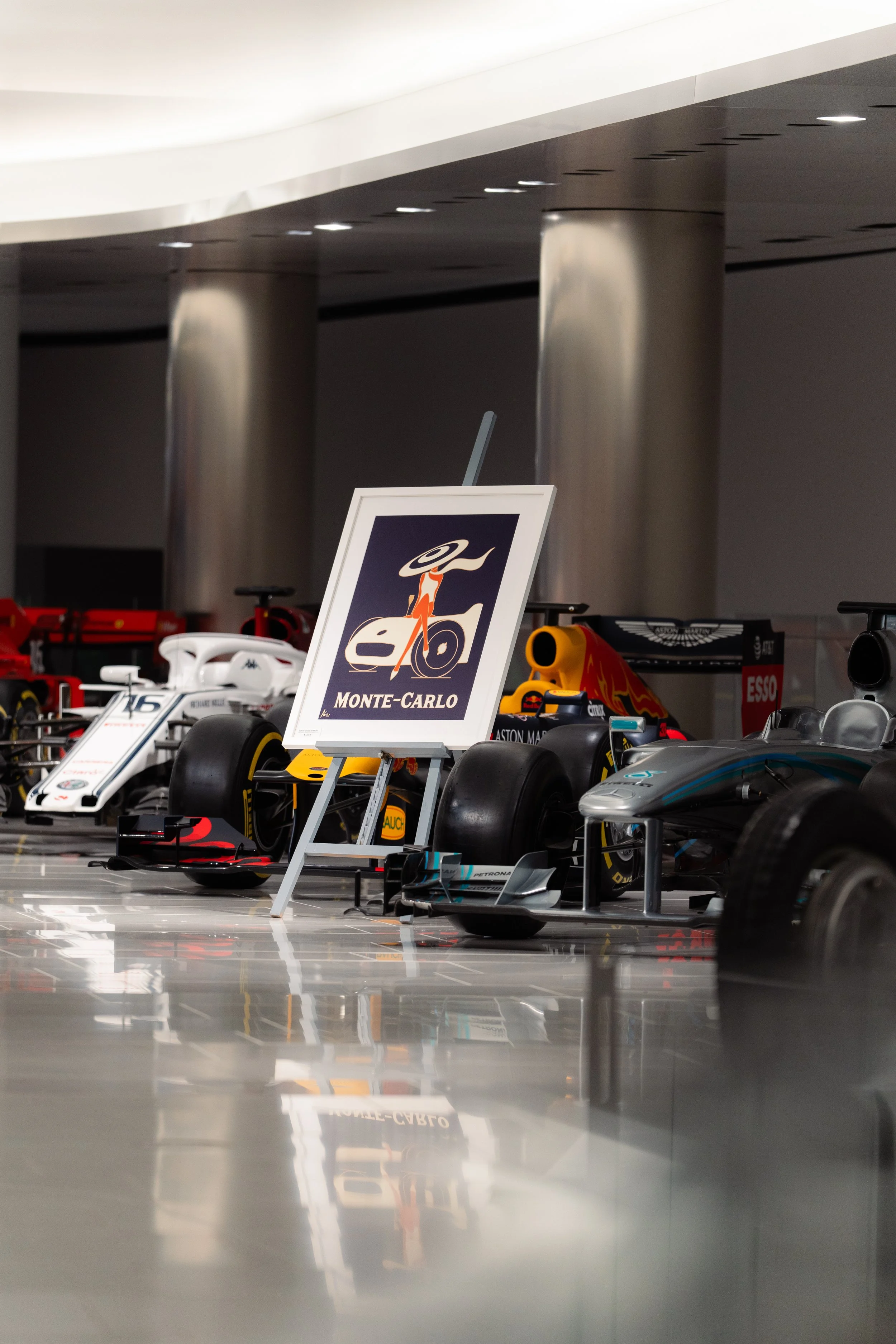 Exposition de voitures de course modernes dans un musée, avec un panneau indiquant Monte-Carlo.