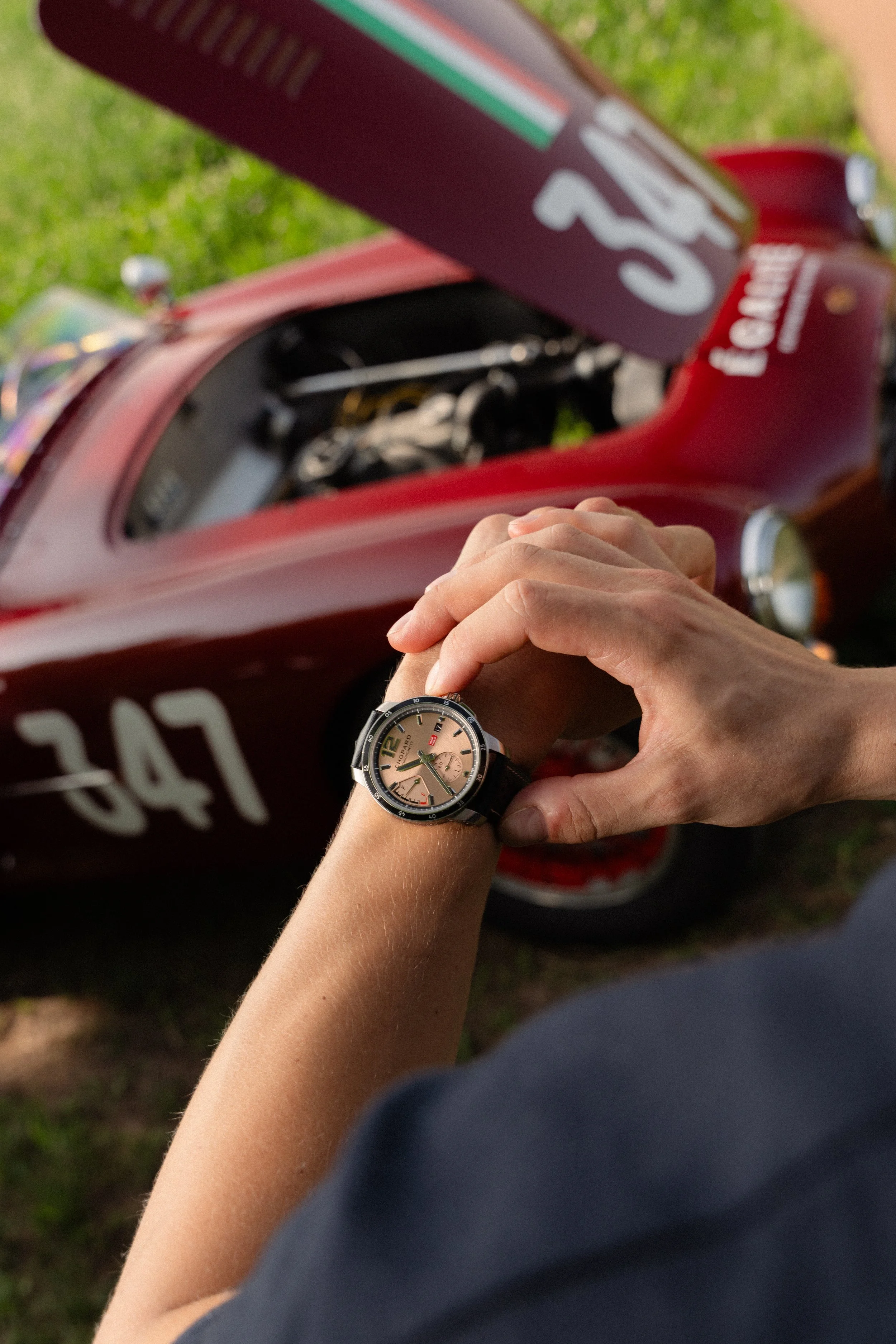 Une personne regarde une montre-bracelet en tenant le poignet devant une voiture de course rouge avec le numéro 047 et une étiquette "ferrari".