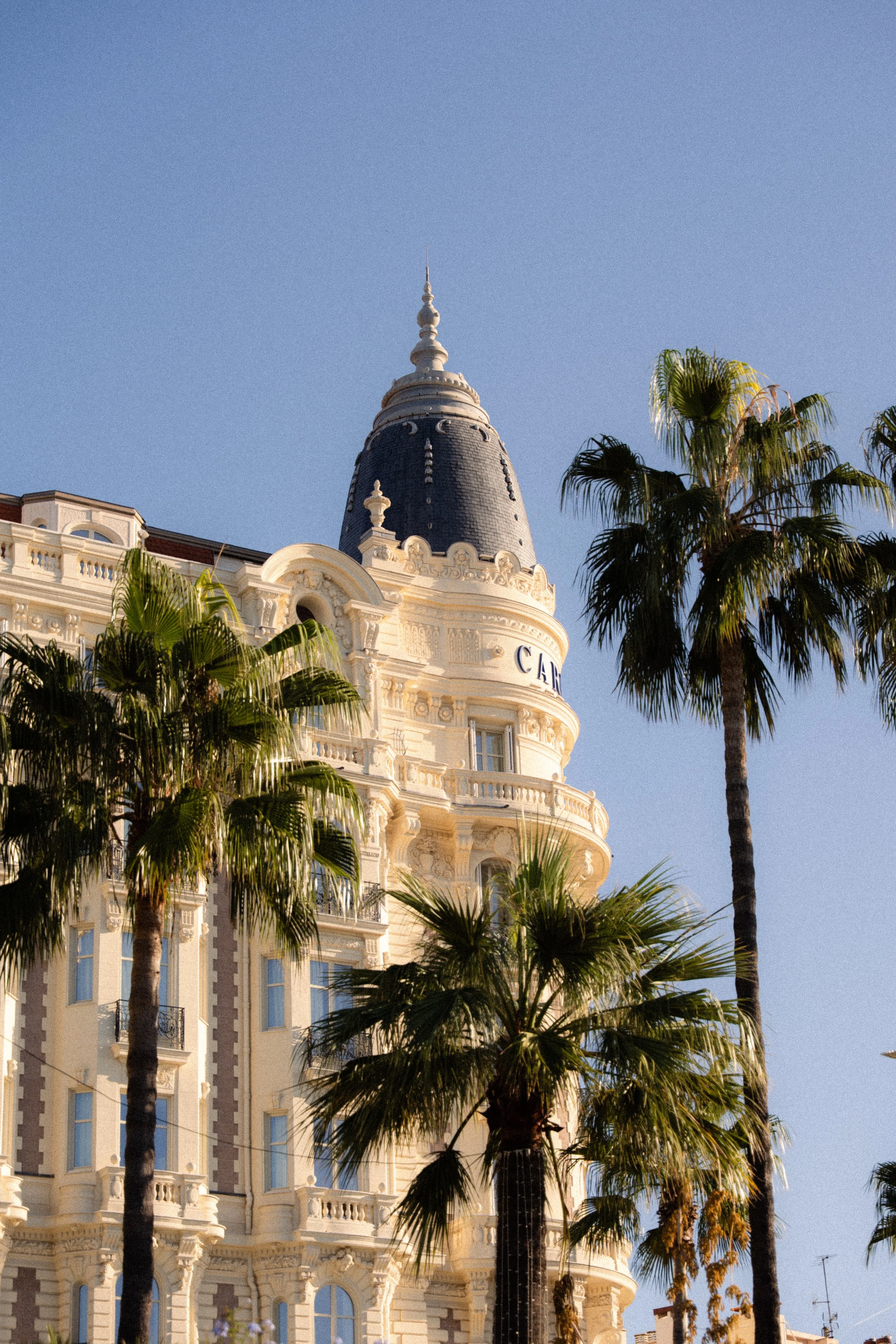 Un bâtiment de style historique avec une coupole bleue et des détails architecturaux élaborés, entouré de palmiers contre un ciel clair.