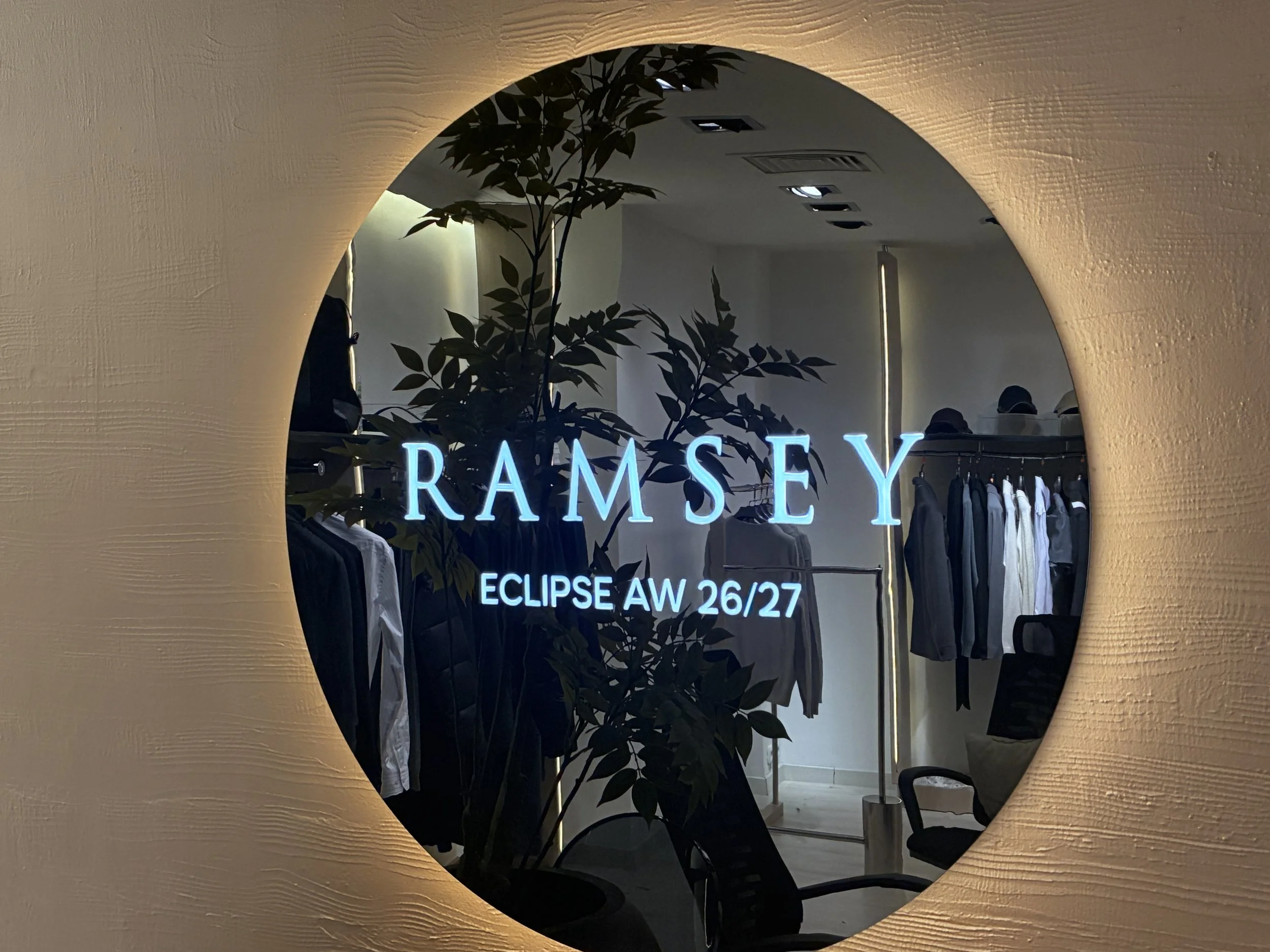Ramsay mağazasının aynasında Eclipse sonbahar ve kış koleksiyonu 26/27 yazısı ile ayna ve içerideki giysi ve oturma alanı görünmektedir.