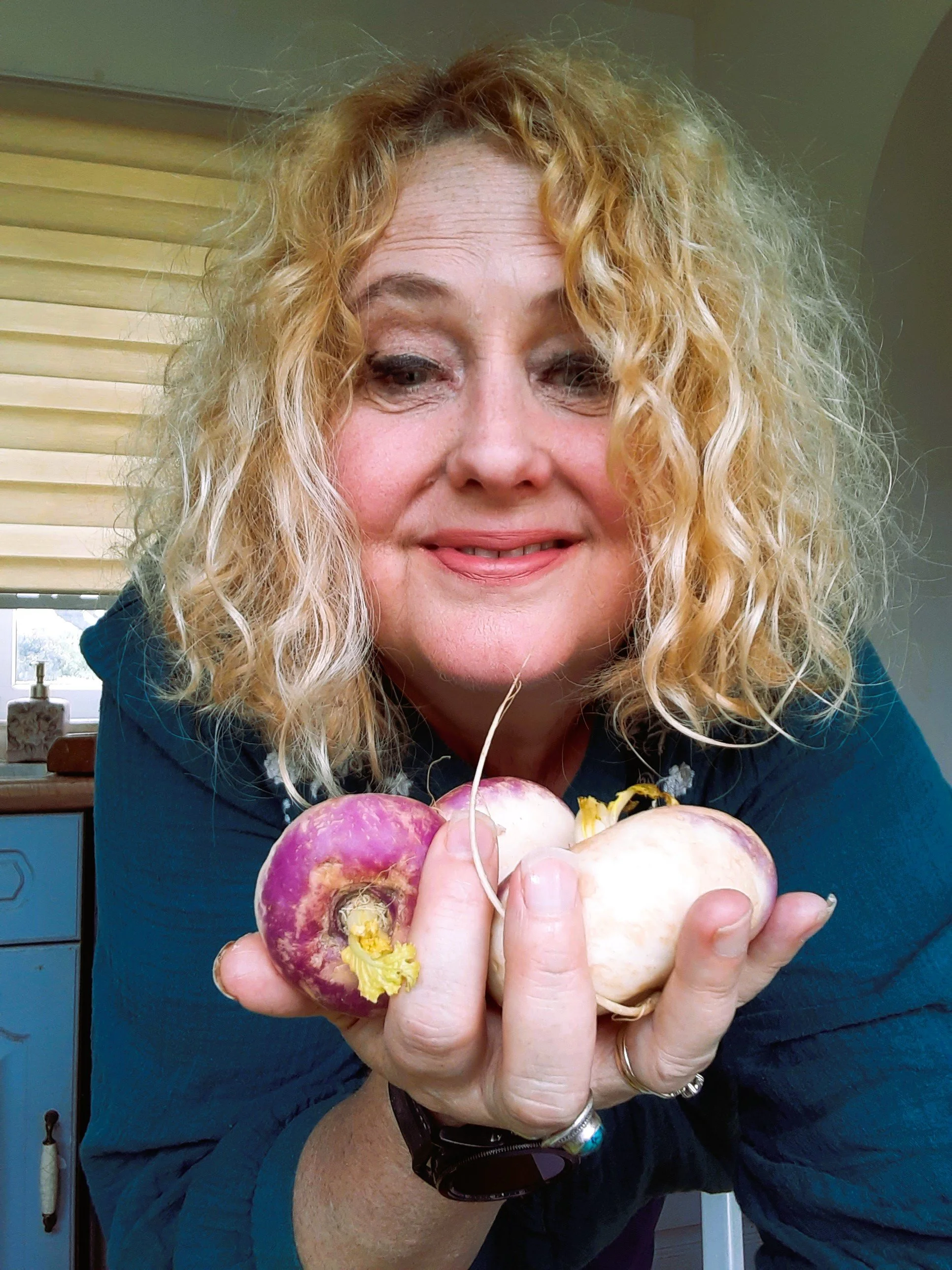 A woman with curly blonde hair smiling and holding a bunch of radishes.
