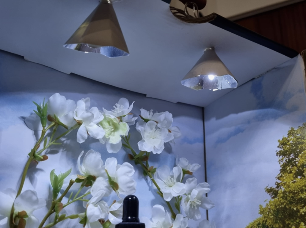 Lighting played a key role in shaping the mood of the display. DIY light fixtures were constructed using small pieces of reflective hard paper to softly direct light toward the product, enhancing its presence without overpowering the scene. Real grav
