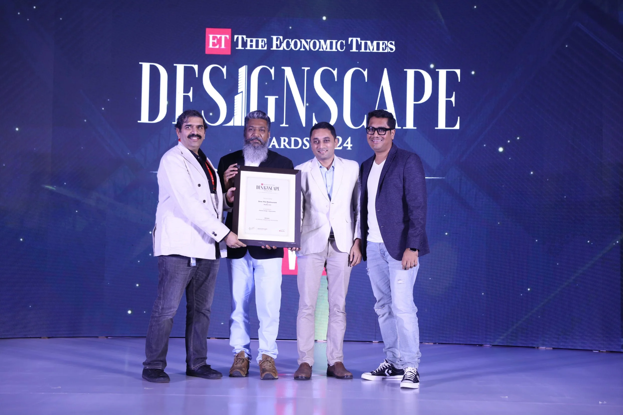 Four men standing on stage holding a framed award at the ET The Economic Times Designscape Awards 2024 event.