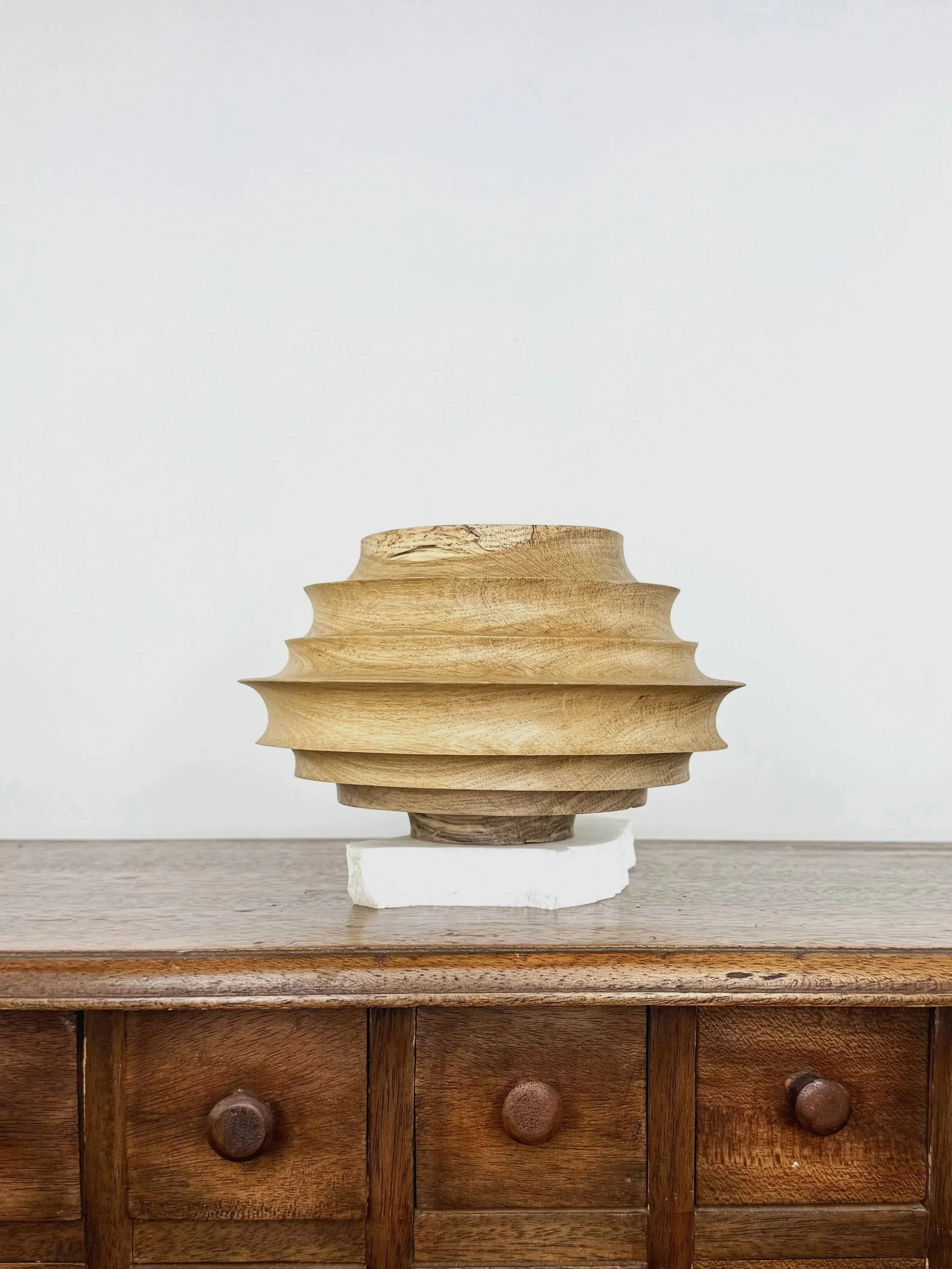 Vase en bois sculpté placé sur une table en bois, contre un mur blanc.