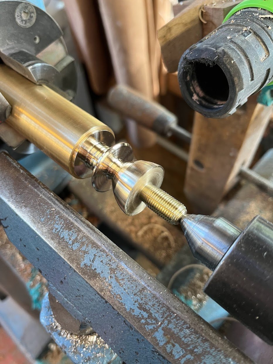 Une pièce en métal est fixée dans un tour à métaux, en cours de fabrication ou de polissage, avec une perceuse électrique à proximité.