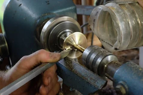 Une personne utilisant une machine pour tourner un objet en métal sur un tour. La main tient un outil contre le métal en rotation.