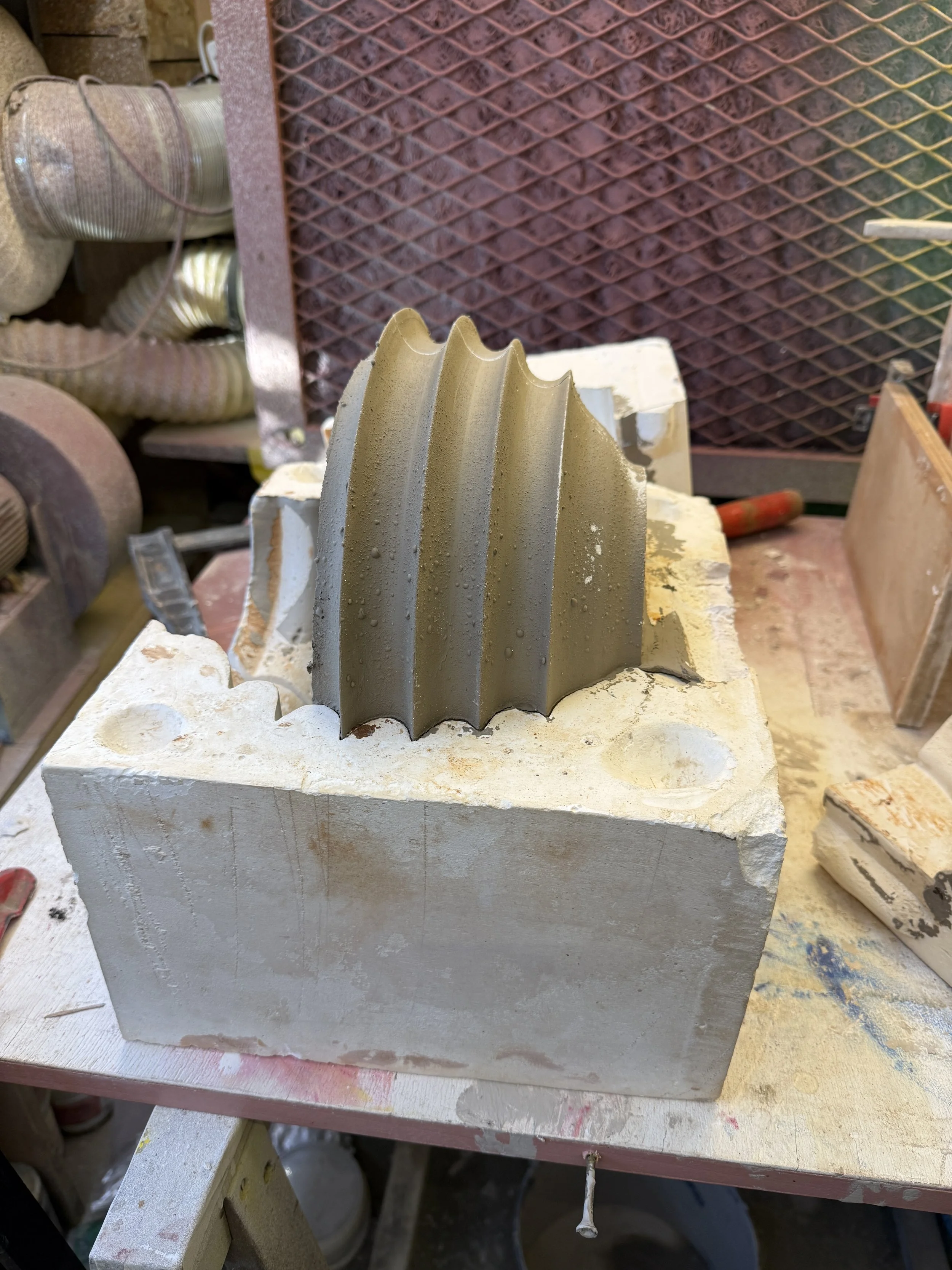 Un moule en plâtre avec une fiche en silicone vert olive, utilisé pour fabriquer un objet en céramique ou en plâtre, posé sur une table de travail.