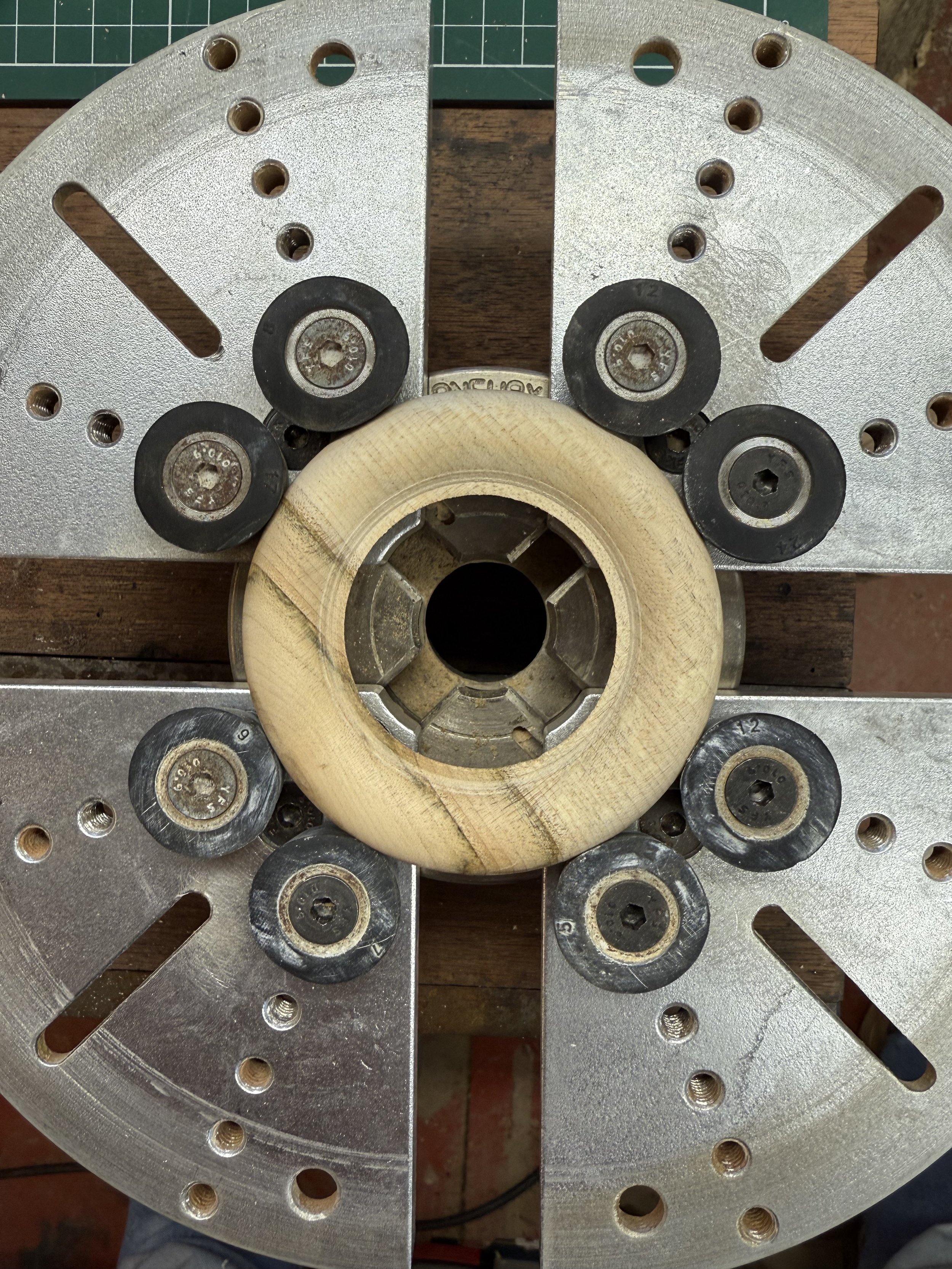 Une pièce mécanique circulaire avec plusieurs roues en caoutchouc, fixée sur une plaque en métal perforée, vue de dessus.