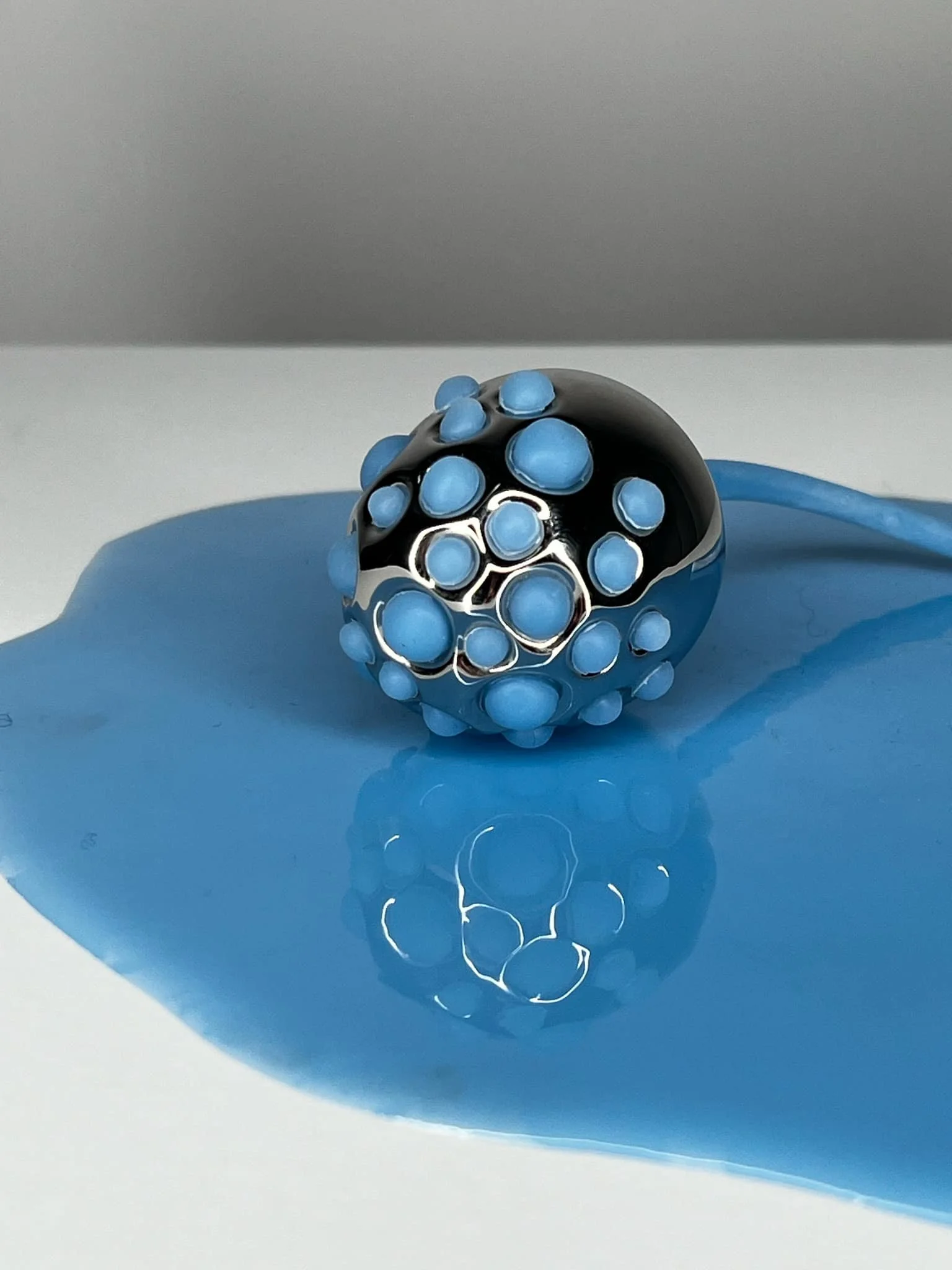 Une sphère métallique décorée de cercles bleus, posée sur une surface bleue qui ressemble à de la peinture étalée.